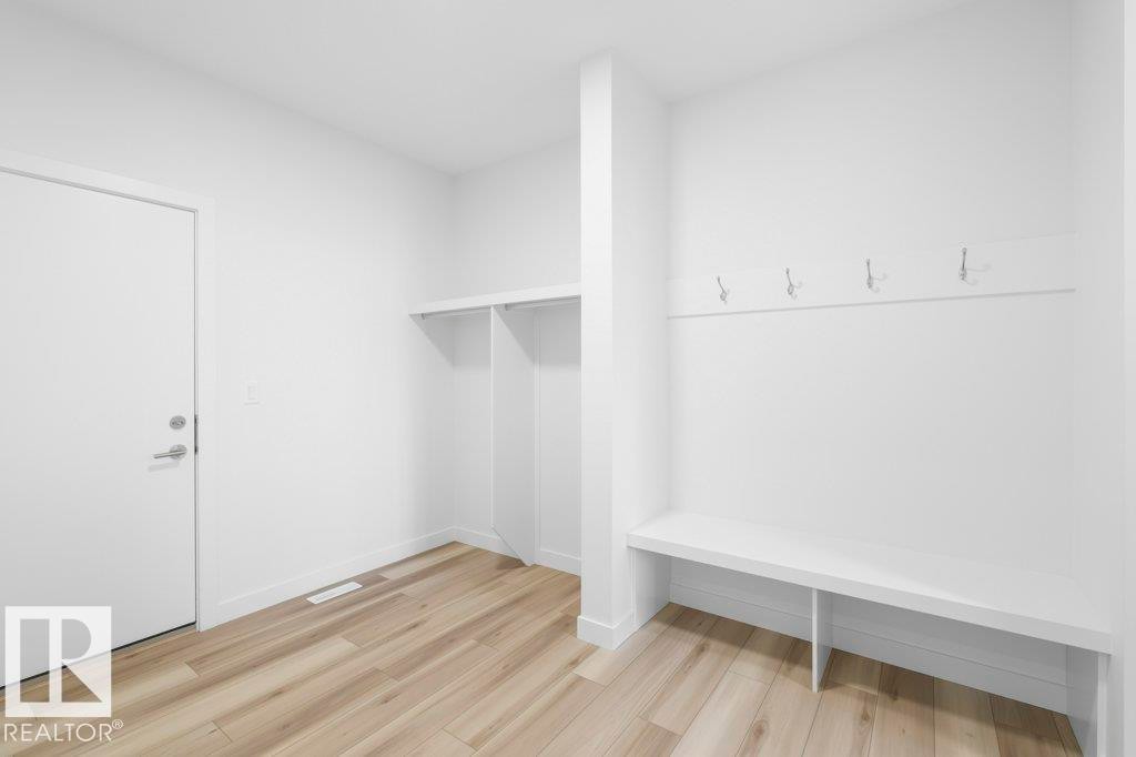 Bright entryway featuring wood-finish flooring, a built-in bench with four wall-mounted hooks, and a built-in storage alcove - 19110 20A Avenue, Edmonton, AB - Indoor