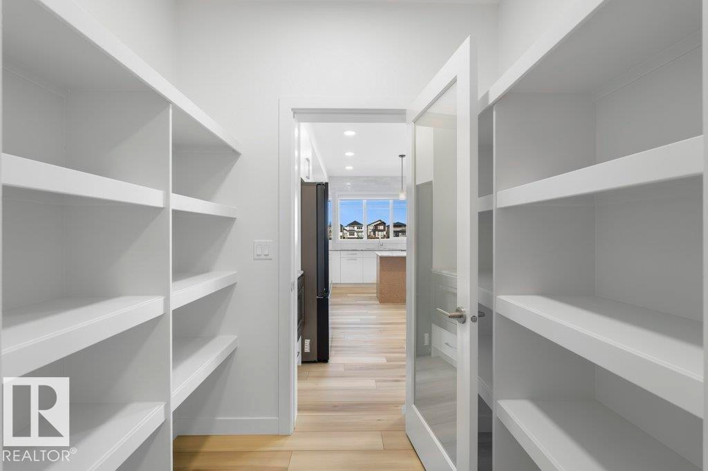 Walk-in pantry featuring extensive built-in shelving, white painted finishes, and wood-finish flooring - 19110 20A Avenue, Edmonton, AB - Indoor With Storage