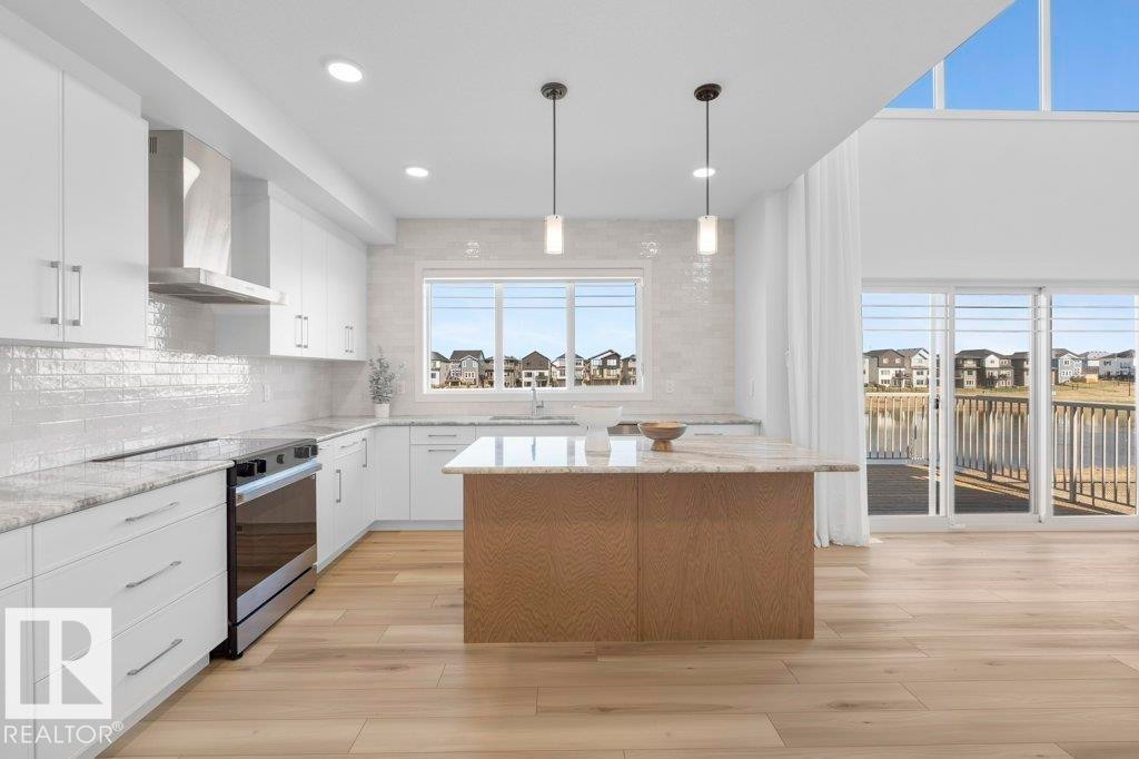 Modern kitchen featuring white cabinetry, stainless steel appliances, a wood-finish island with a light-colored countertop, recessed lighting, and wood-finish flooring - 19110 20A Avenue, Edmonton, AB - Indoor Photo Showing Kitchen With Upgraded Kitchen