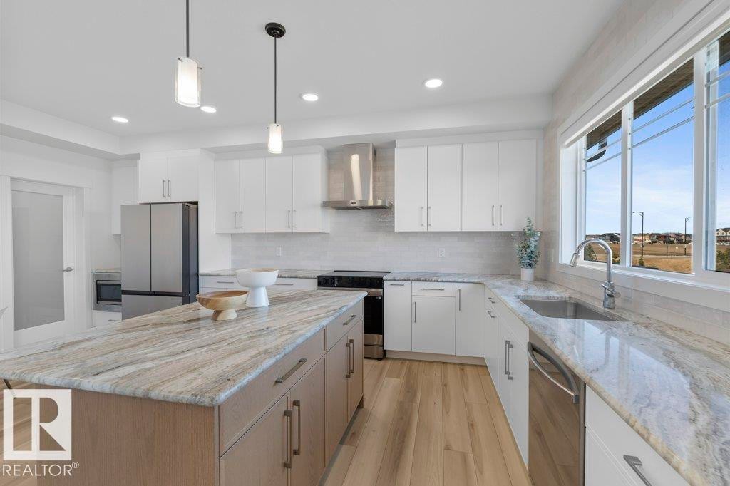 Bright kitchen featuring a central island with a light wood-finish base and a stone-finish countertop - 19110 20A Avenue, Edmonton, AB - Indoor Photo Showing Kitchen With Upgraded Kitchen