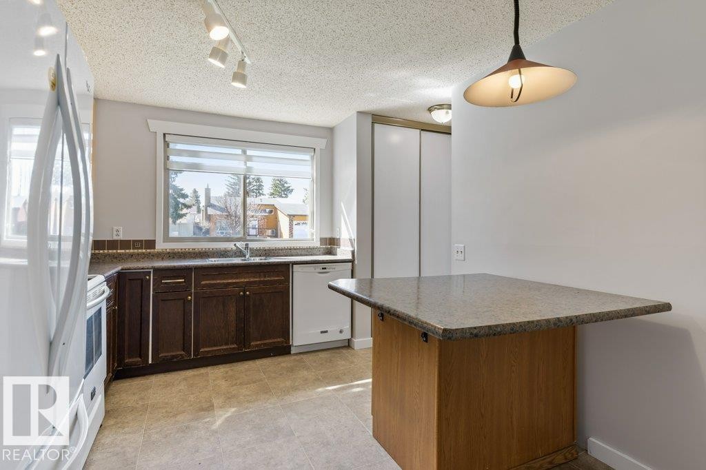 Kitchen featuring dark wood cabinetry, a light-toned countertop, and a mosaic tile backsplash - 3736 12 Avenue, Edmonton, AB - Indoor Photo Showing Kitchen With Double Sink