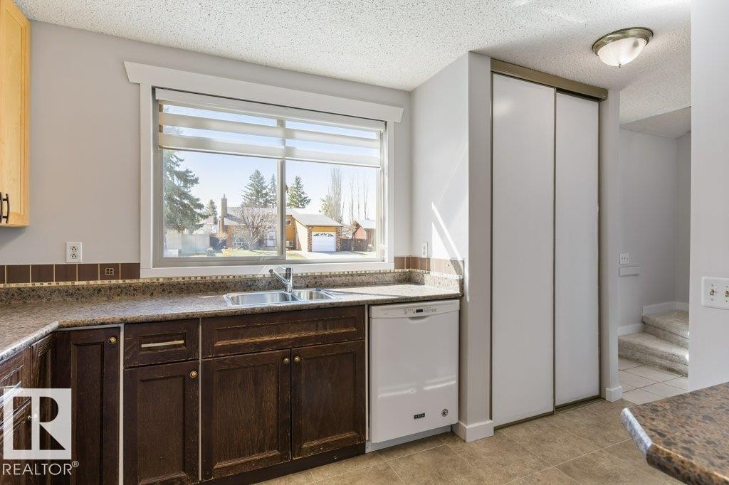 Kitchen featuring dark wood-finish cabinetry, light wood-finish upper cabinetry, a stainless steel sink, a white dishwasher, and stone-finish countertops with a mosaic tile backsplash - 3736 12 Avenue, Edmonton, AB - Indoor Photo Showing Kitchen