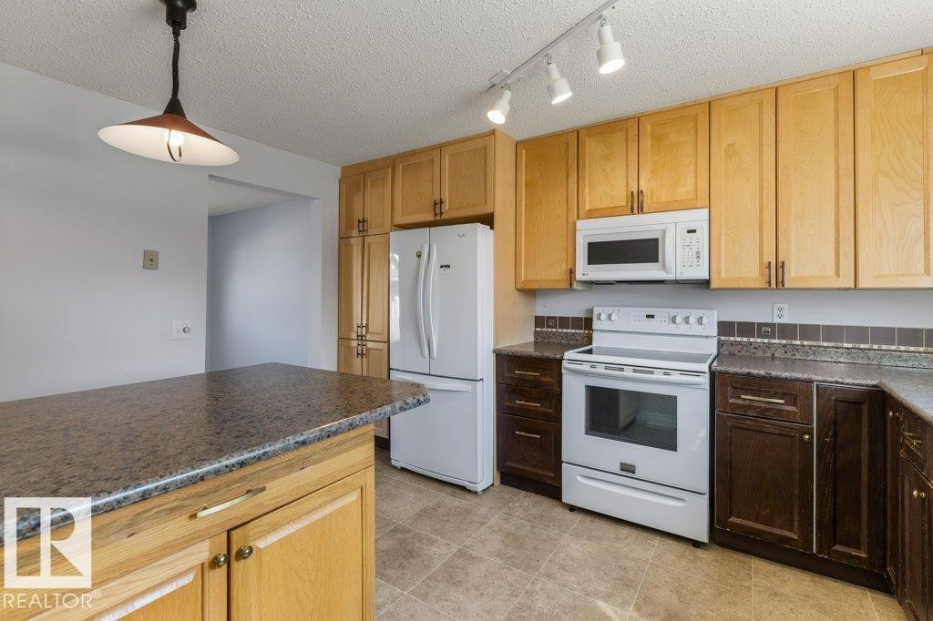Kitchen featuring an island with a stone-finish countertop, light wood cabinetry, and a pendant light fixture - 3736 12 Avenue, Edmonton, AB - Indoor Photo Showing Kitchen