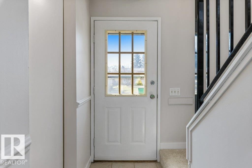 Entryway featuring a white paneled door with divided lite window, light-colored tile flooring, and a carpeted staircase with dark balusters - 3736 12 Avenue, Edmonton, AB - Indoor Photo Showing Other Room