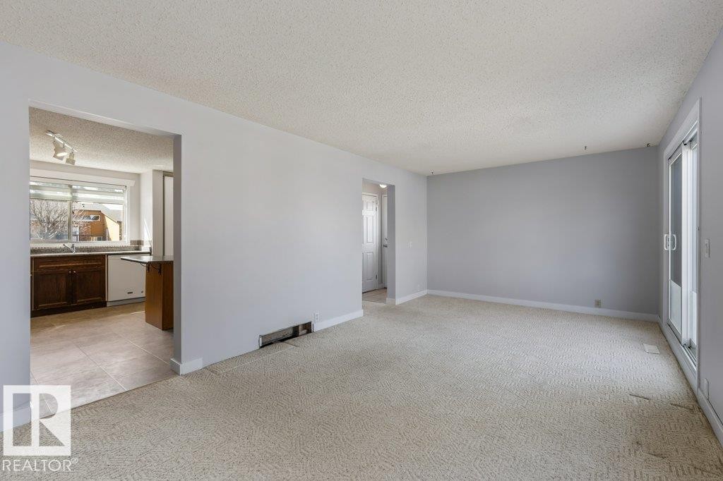 Spacious living area with neutral carpeting, light gray wall paint, and a textured ceiling - 3736 12 Avenue, Edmonton, AB - Indoor Photo Showing Other Room