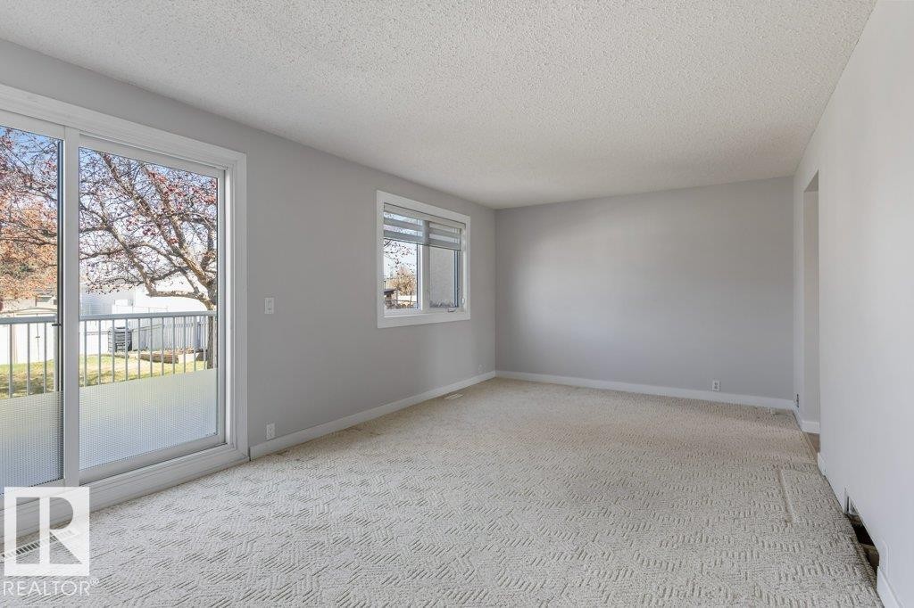 Spacious room featuring light gray wall paint, textured carpet, and a large sliding glass door opening to an exterior balcony - 3736 12 Avenue, Edmonton, AB - Indoor Photo Showing Other Room