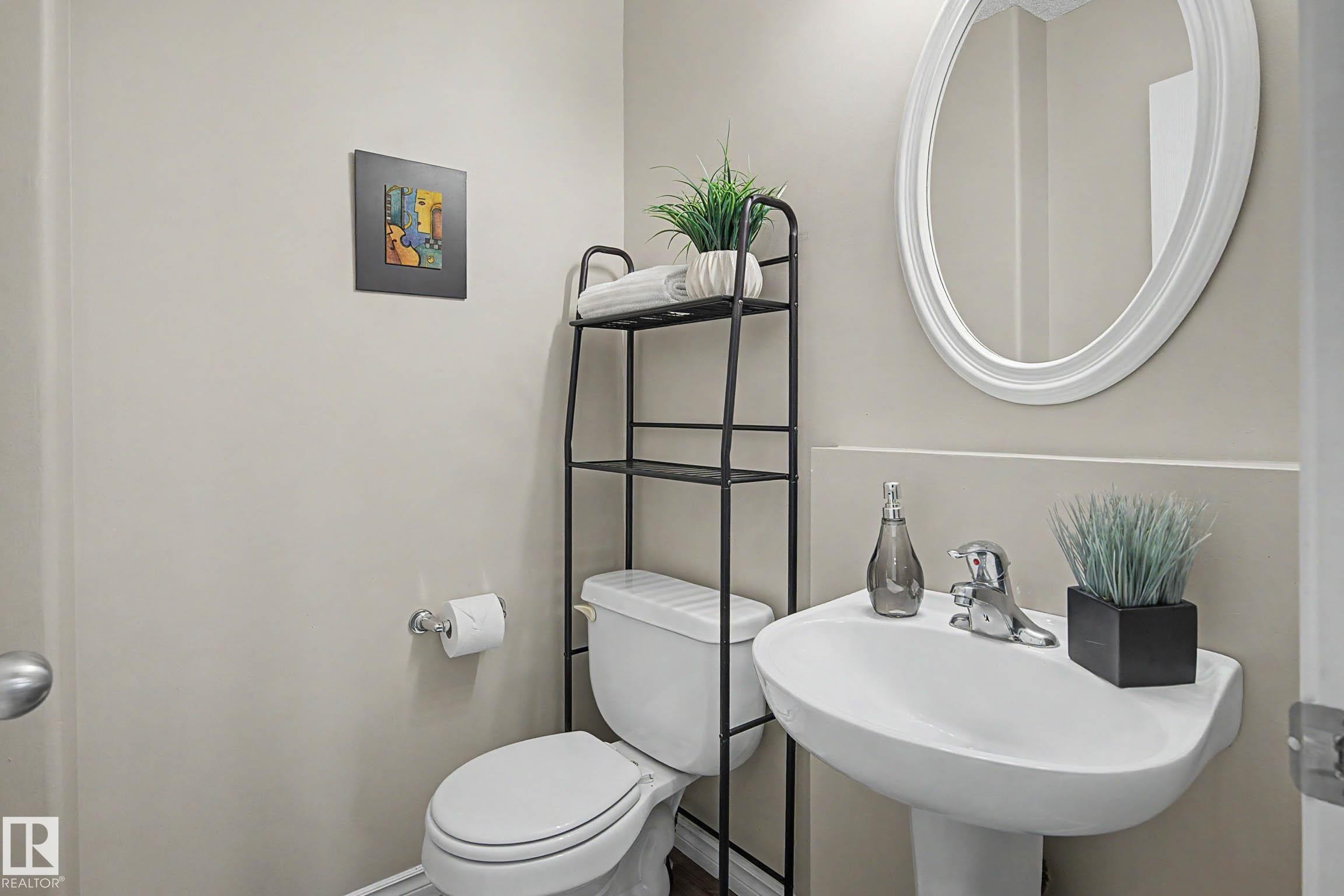 Pedestal sink with chrome faucet and an oval-framed mirror - 7723 7A Avenue, Edmonton, AB - Indoor Photo Showing Bathroom