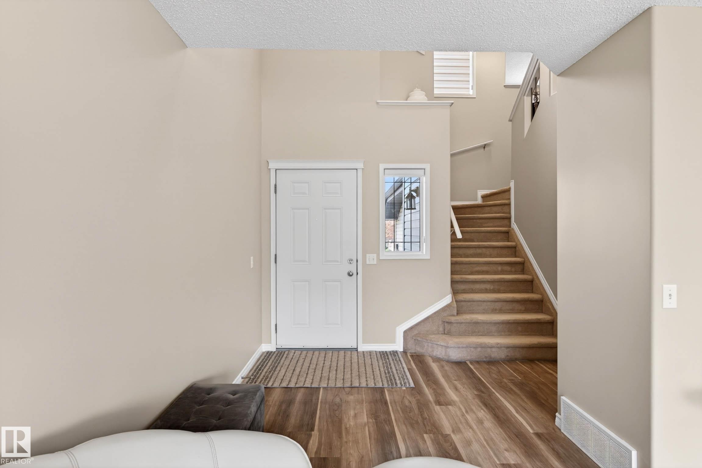 Entryway featuring a paneled door with an adjacent sidelight window, wood-finish flooring, and a carpeted staircase with white trim - 7723 7A Avenue, Edmonton, AB - Indoor Photo Showing Other Room