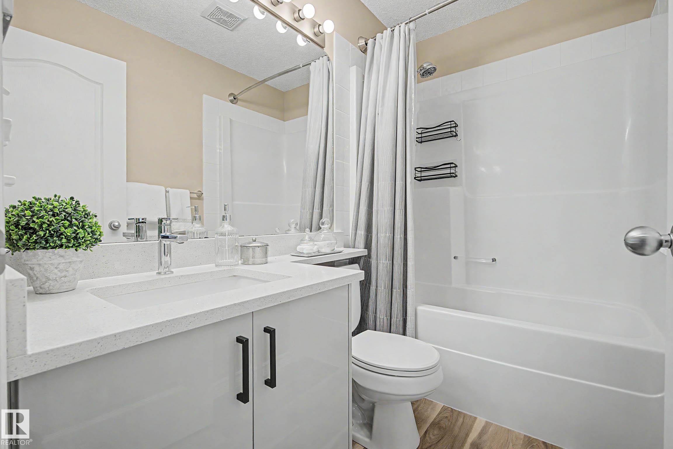 Bathroom featuring a white vanity with a rectangular integrated sink, chrome faucet, and dark cabinet pulls - 7723 7A Avenue, Edmonton, AB - Indoor Photo Showing Bathroom