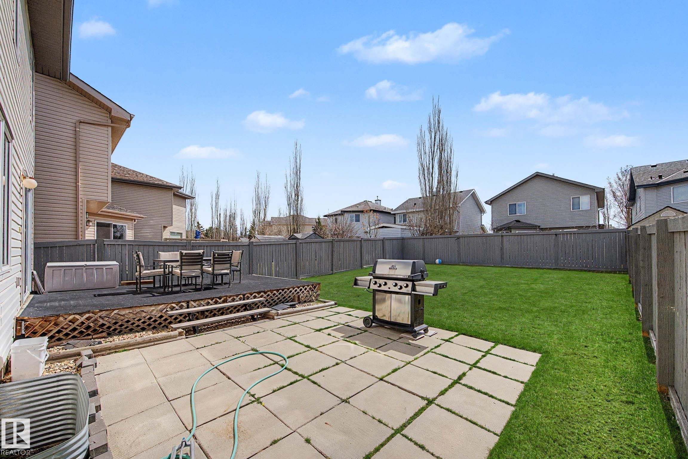 Expansive backyard featuring a manicured lawn, full privacy fencing, and a multi-level outdoor living space - 7723 7A Avenue, Edmonton, AB - Outdoor With Deck Patio Veranda