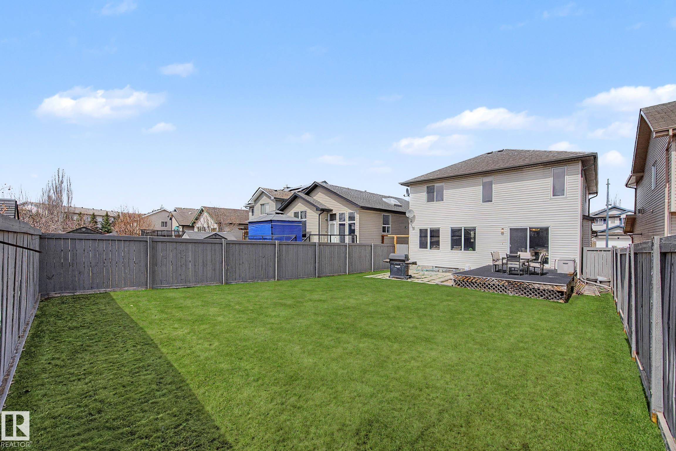 Expansive backyard featuring a manicured lawn, full privacy fencing, and a wooden deck - 7723 7A Avenue, Edmonton, AB - Outdoor