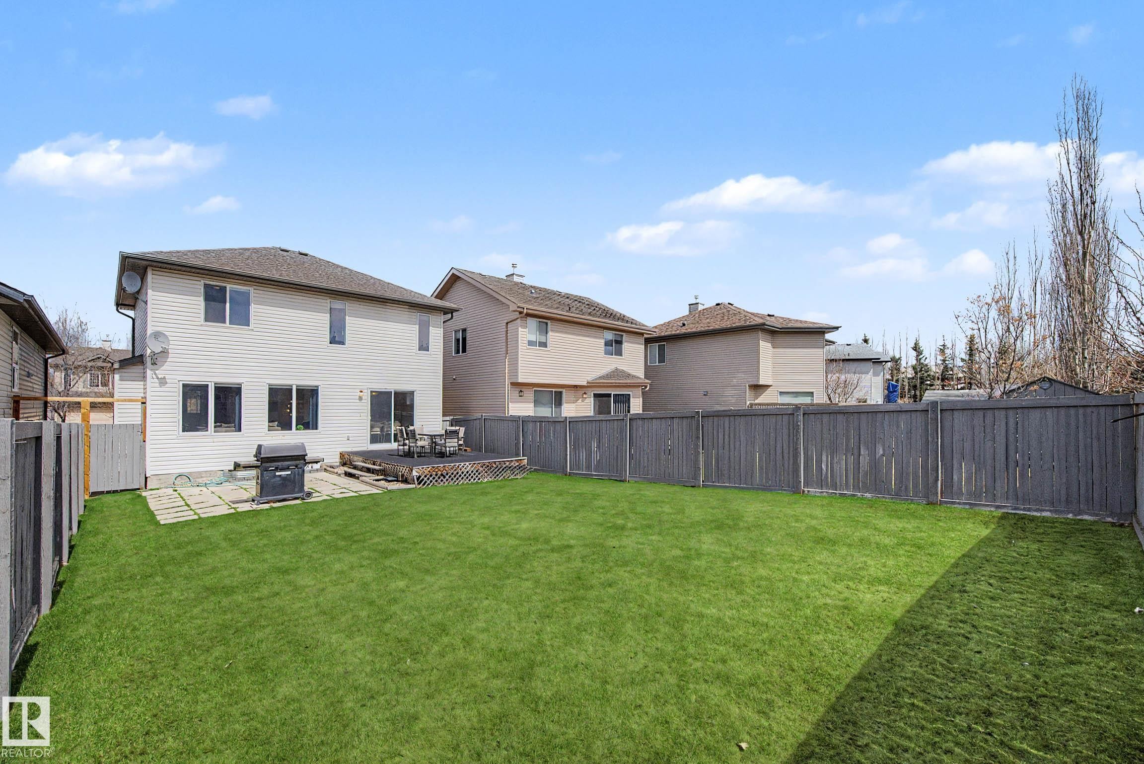 Expansive backyard featuring a large green lawn, a wooden deck, and a patio area - 7723 7A Avenue, Edmonton, AB - Outdoor With Backyard
