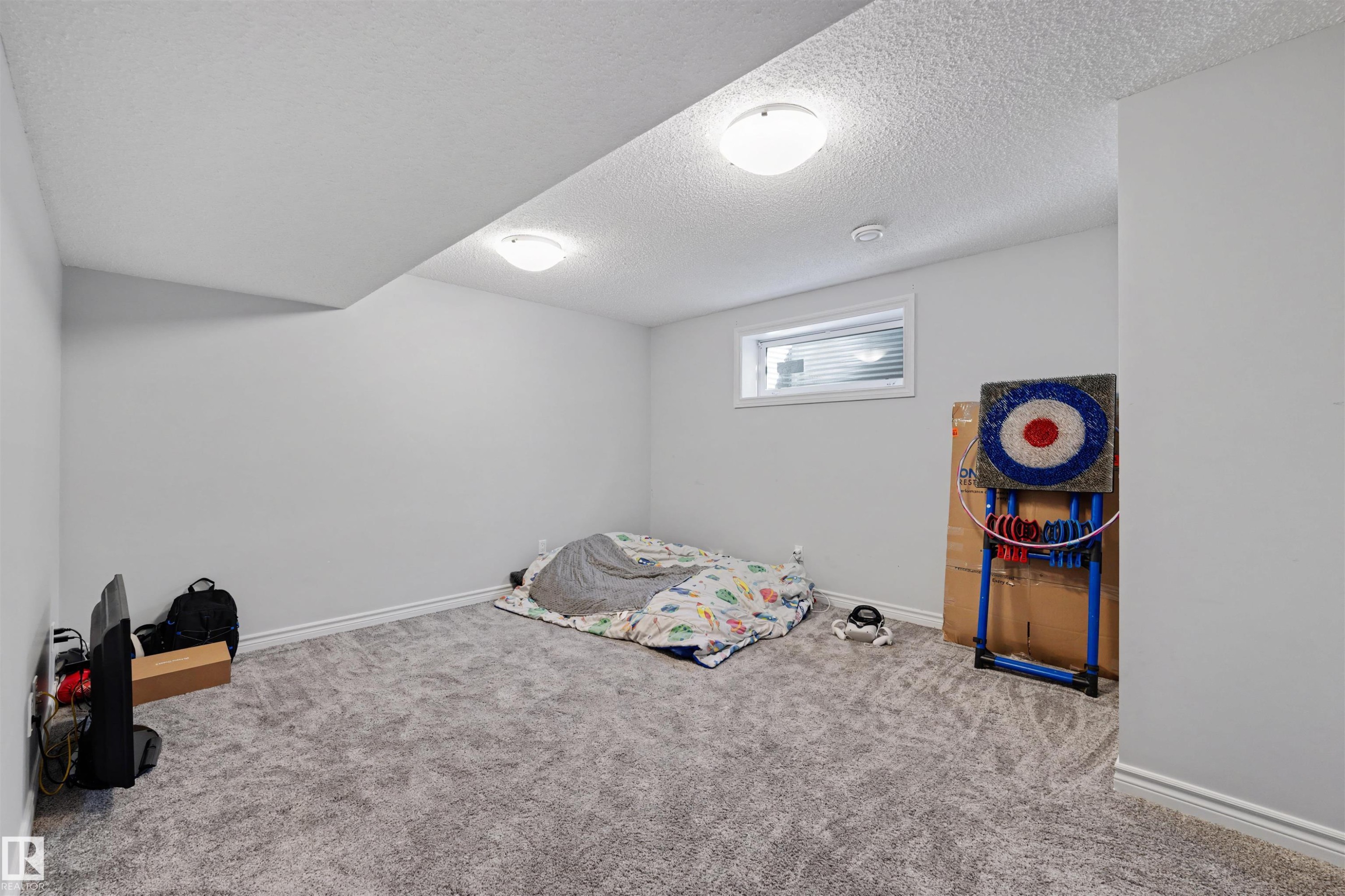 Spacious room featuring light gray walls, textured ceiling, two ceiling-mounted dome lights, and gray patterned carpeting - 6115 18 Avenue, Edmonton, AB - Indoor Photo Showing Bedroom