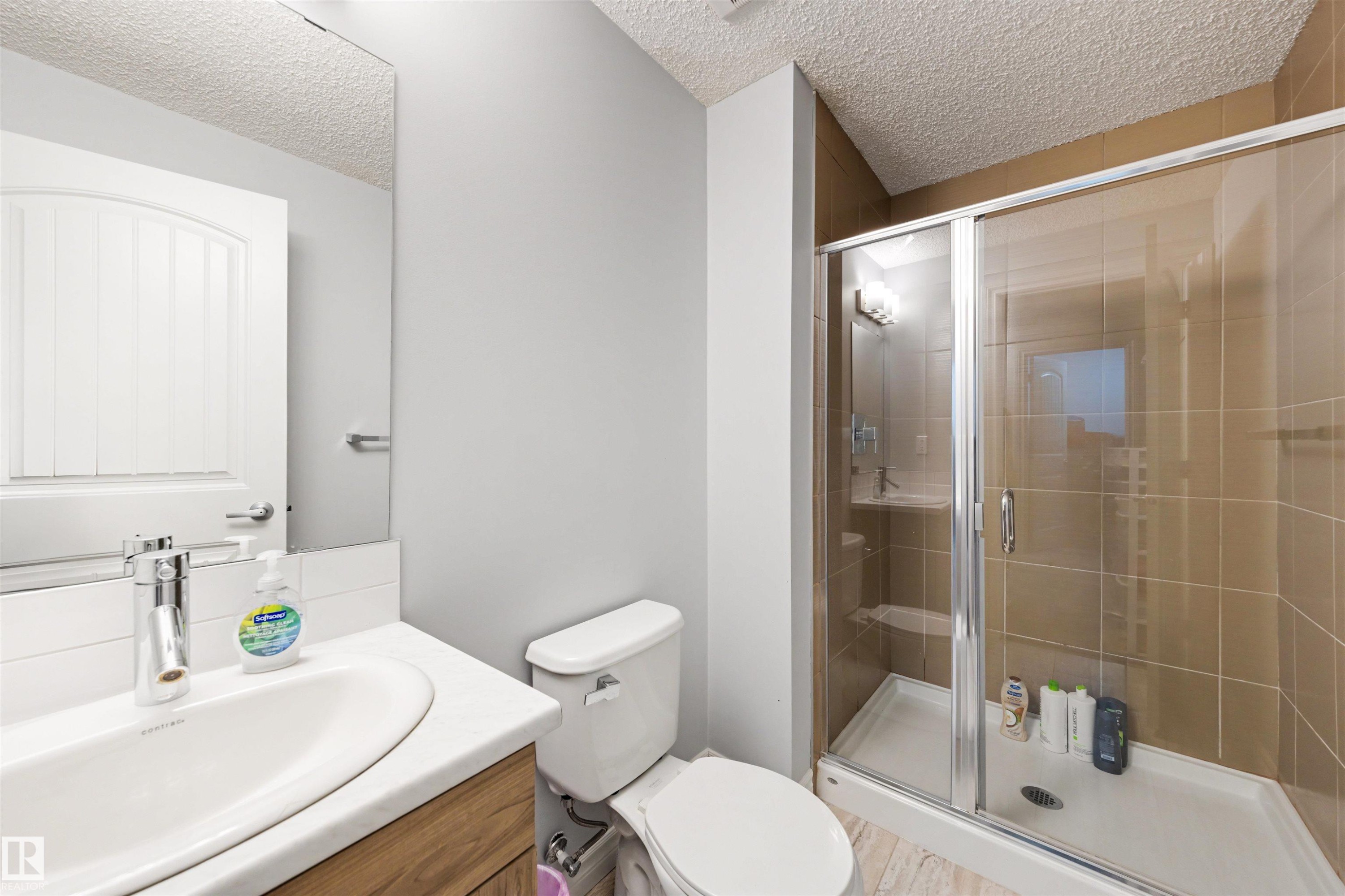 Full bathroom featuring a glass-enclosed shower with tile surround, a built-in shower bench, a vanity with an undermount sink, and wood-finish cabinetry - 6115 18 Avenue, Edmonton, AB - Indoor Photo Showing Bathroom