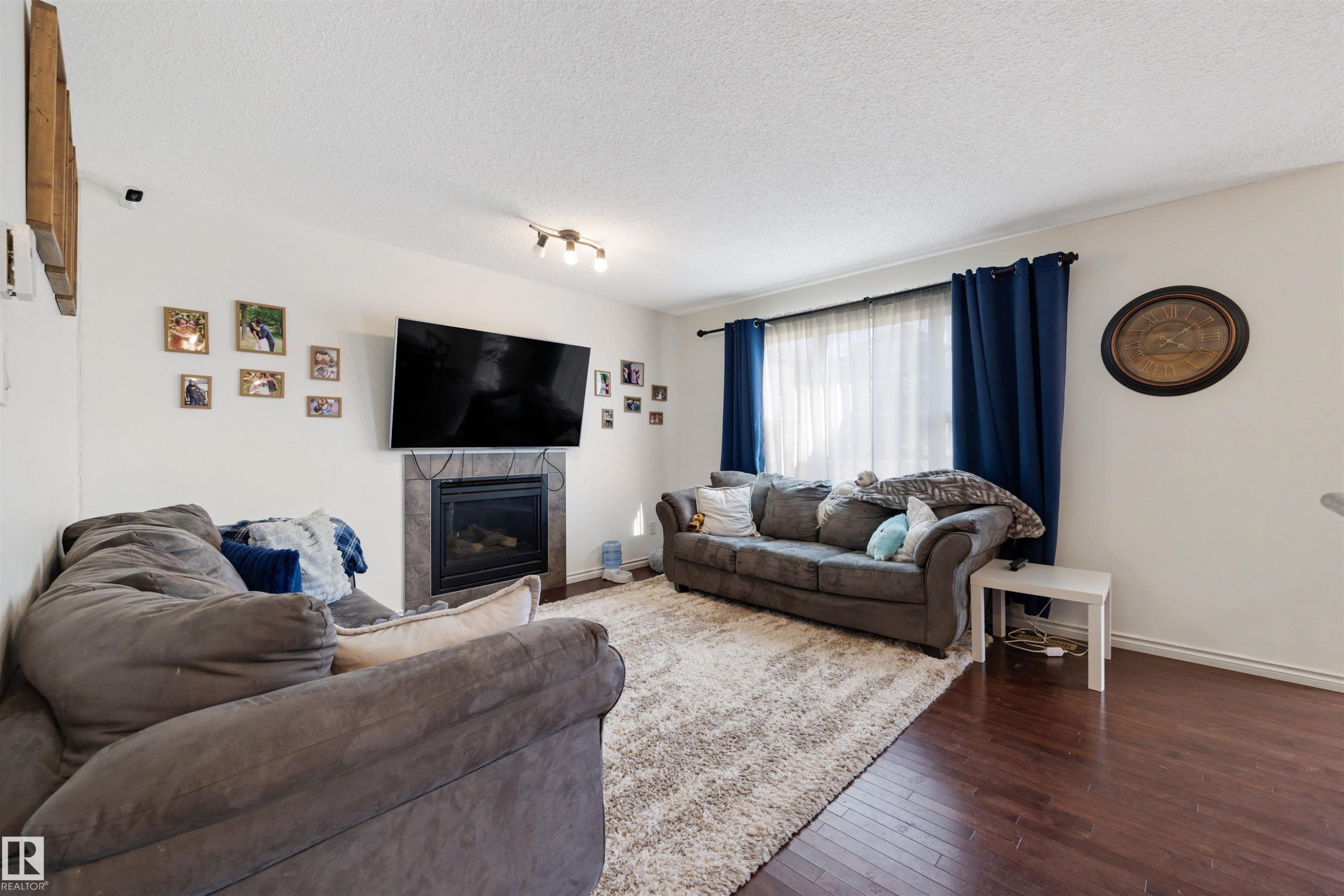 Living area featuring wood-finish flooring, a built-in fireplace with a stone surround, and a ceiling-mounted light fixture - 6115 18 Avenue, Edmonton, AB - Indoor Photo Showing Living Room With Fireplace