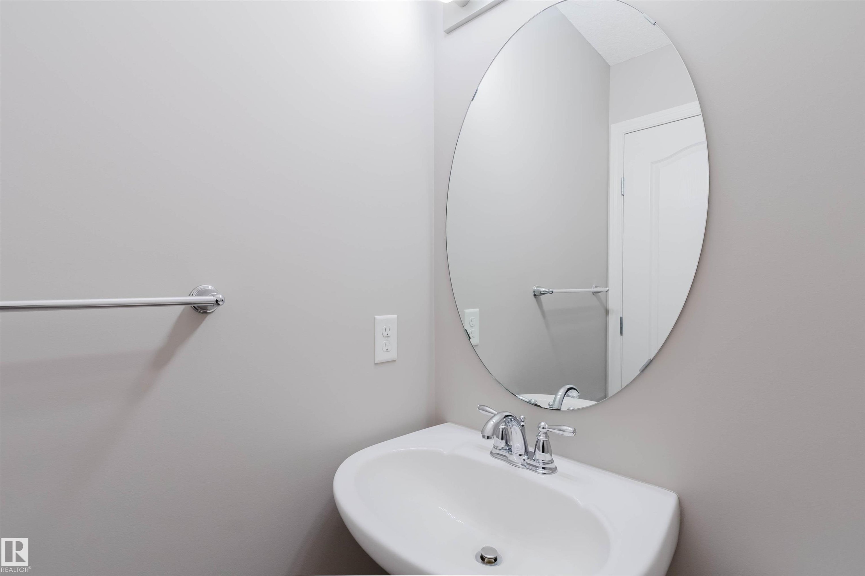 Pedestal sink featuring a chrome faucet, oval mirror, and wall-mounted towel bar - 16627 18 Avenue, Edmonton, AB - Indoor Photo Showing Bathroom