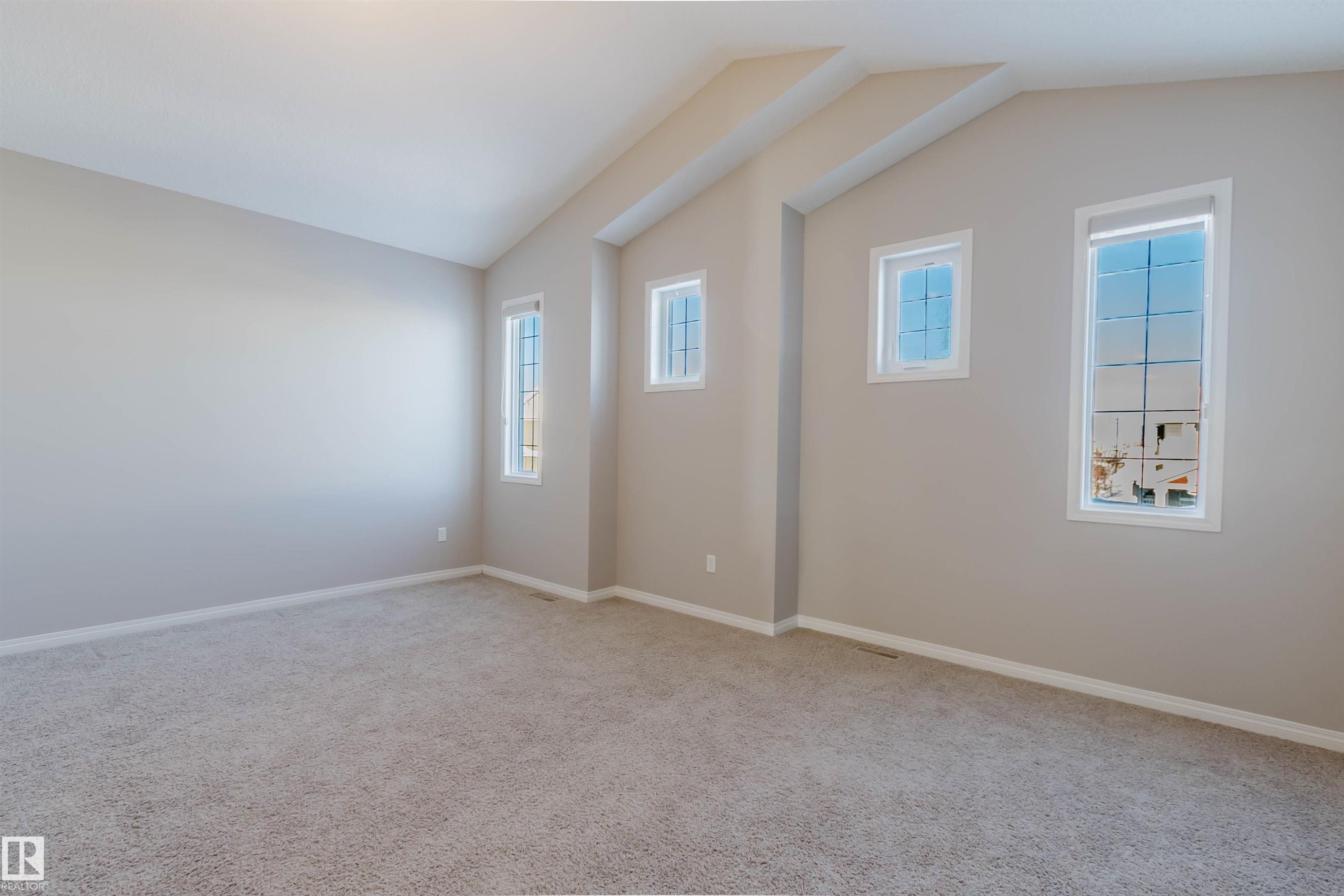 Spacious room featuring vaulted ceilings, light neutral wall tones, plush carpet flooring, and multiple window openings - 16627 18 Avenue, Edmonton, AB - Indoor Photo Showing Other Room