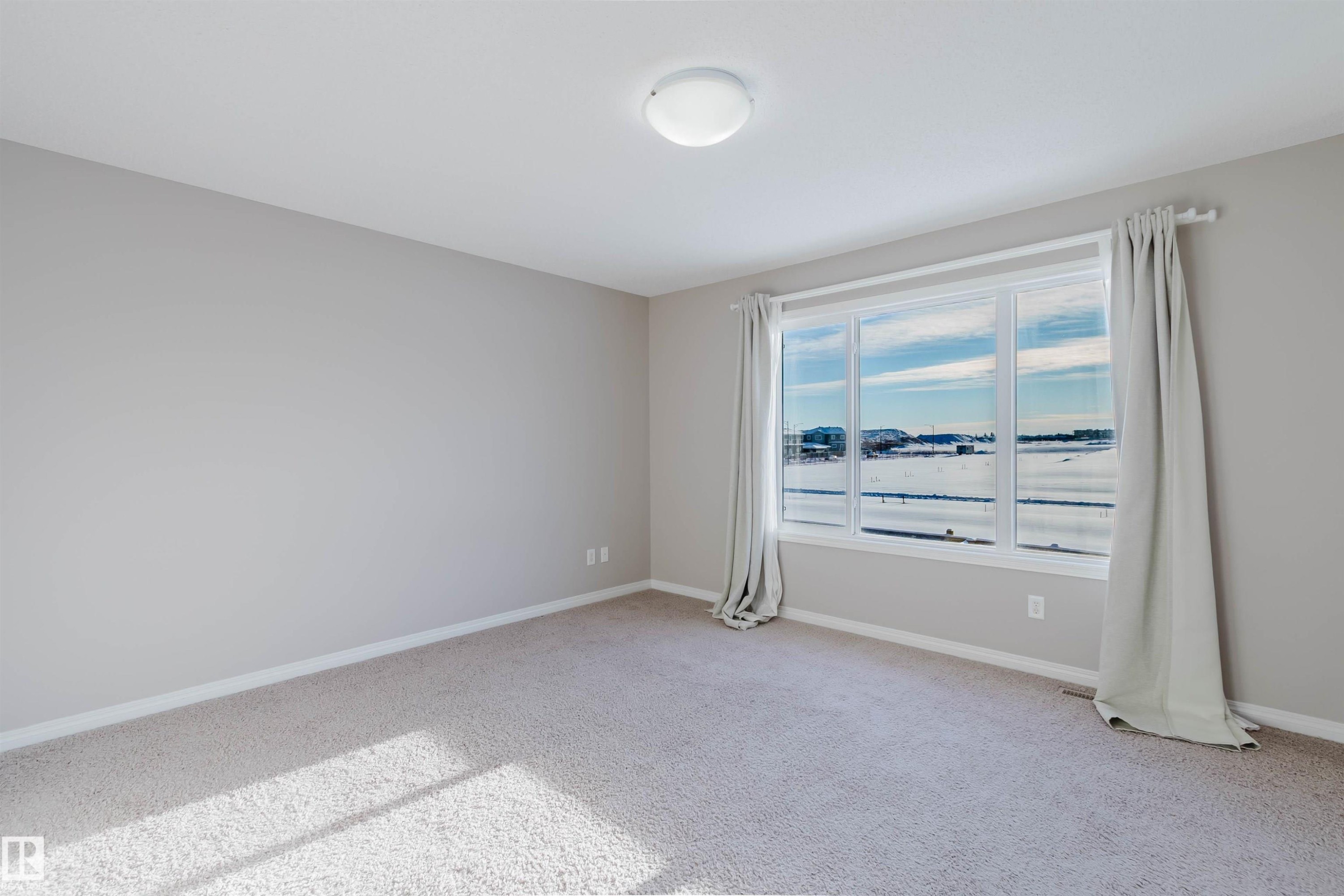 Bright room featuring a large multi-pane window, neutral-toned walls, light carpeting, and a flush-mount ceiling light - 16627 18 Avenue, Edmonton, AB - Indoor Photo Showing Other Room