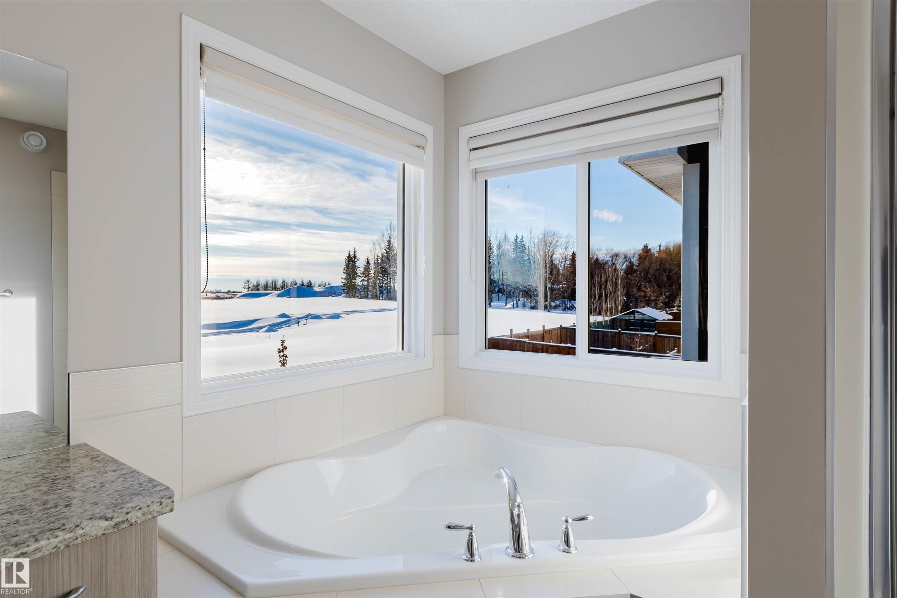 Corner soaking tub with polished chrome fixtures and surrounding white tile - 16627 18 Avenue, Edmonton, AB - Indoor Photo Showing Bathroom