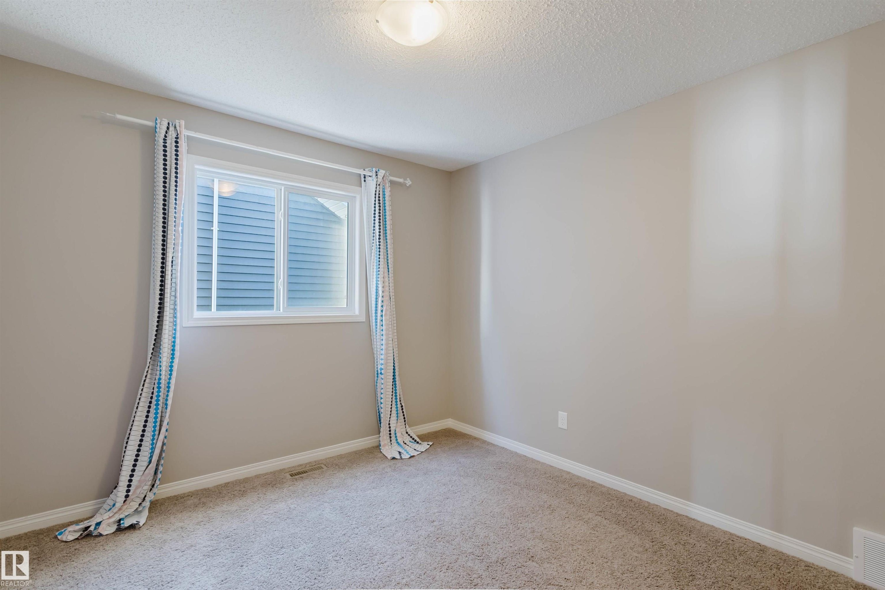 Bright room featuring a window with white trim, light neutral wall paint, white baseboards, and textured carpeting - 16627 18 Avenue, Edmonton, AB - Indoor Photo Showing Other Room