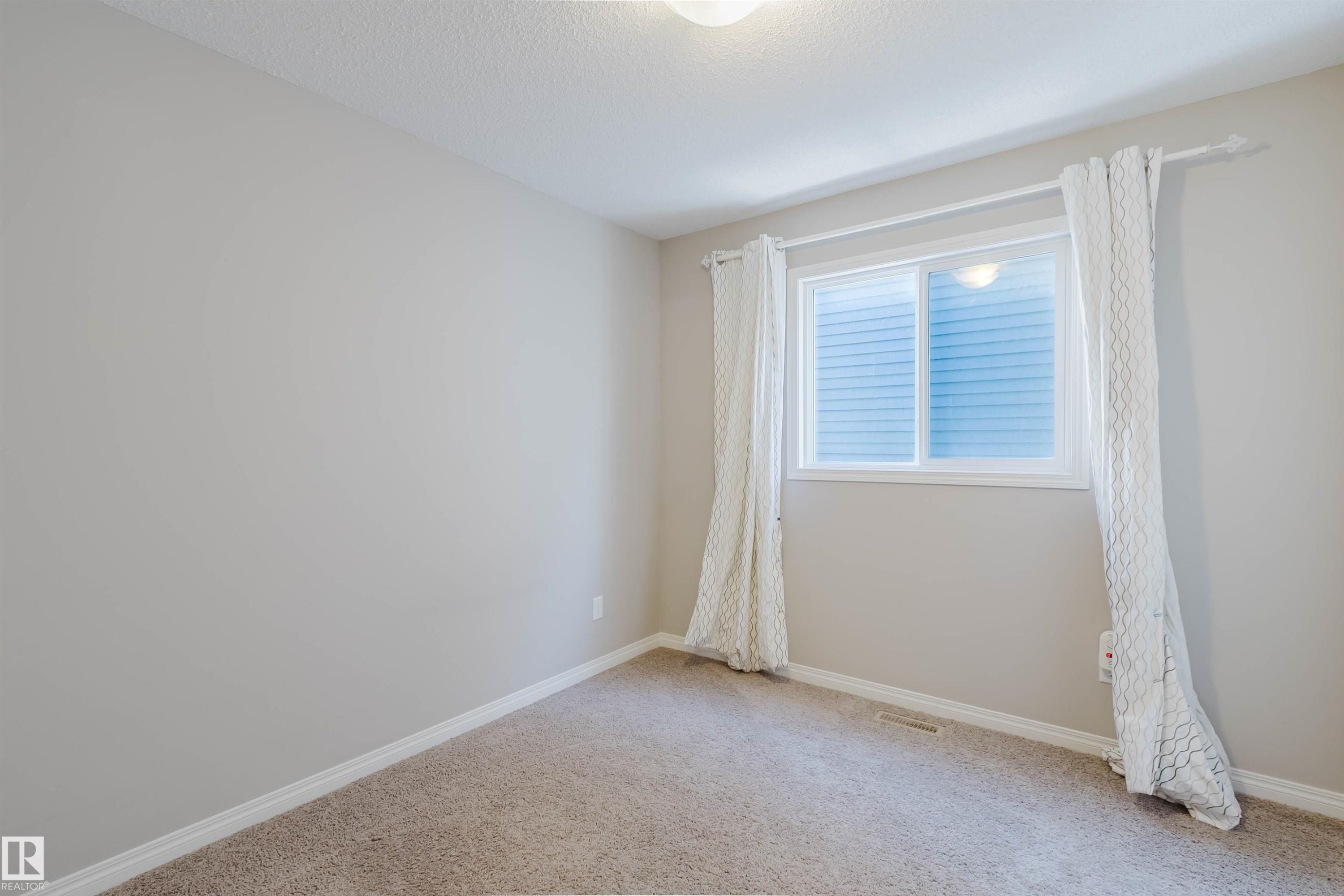 Carpeted room featuring a window with white blinds, a ceiling-mounted light fixture, white baseboards, and neutral wall paint - 16627 18 Avenue, Edmonton, AB - Indoor