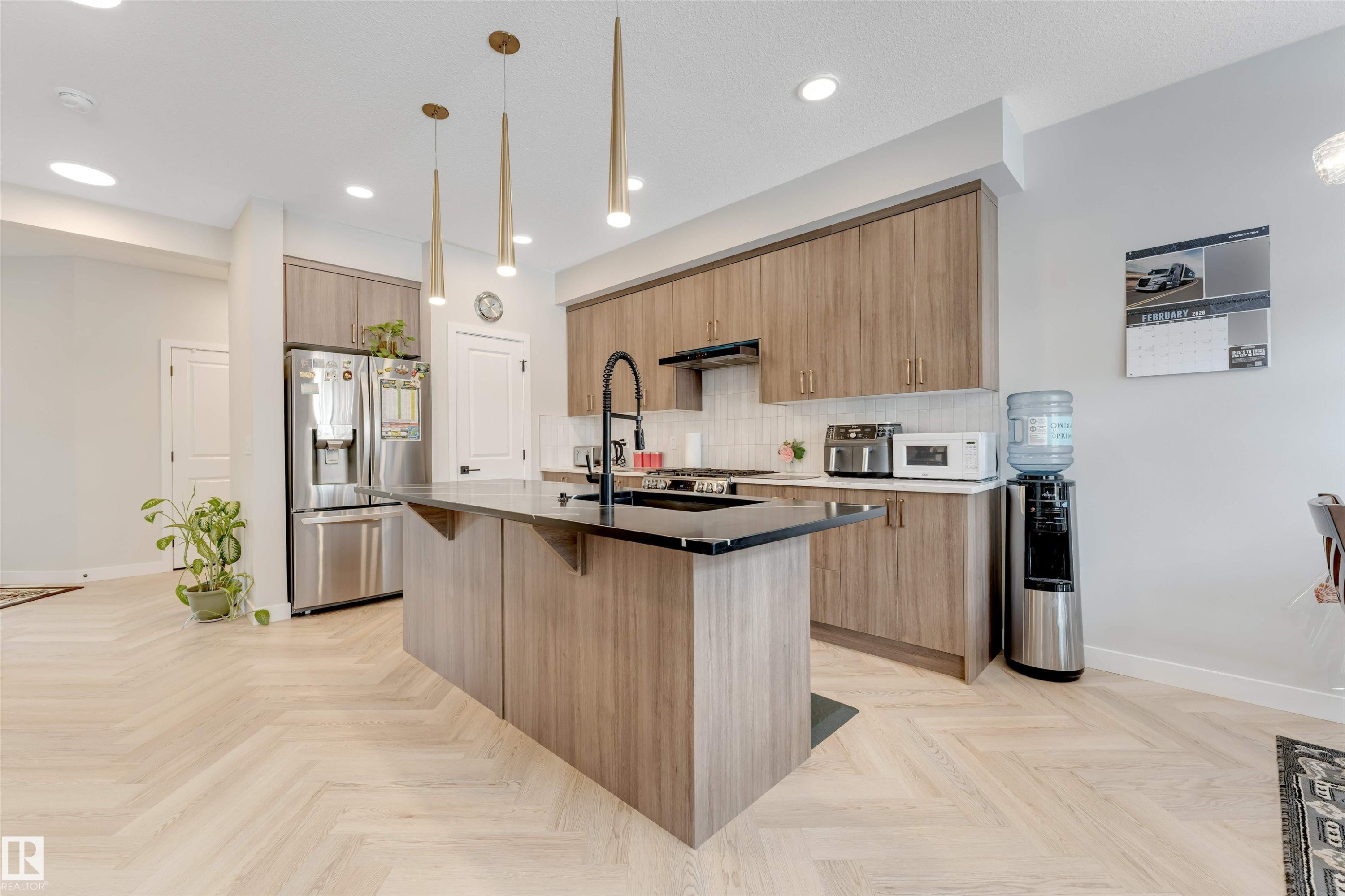 Kitchen featuring an island with a black countertop, herringbone wood-finish flooring, recessed lighting, brass pendant lighting, and stainless steel appliances - 6404 27 Avenue, Edmonton, AB - Indoor Photo Showing Kitchen With Upgraded Kitchen