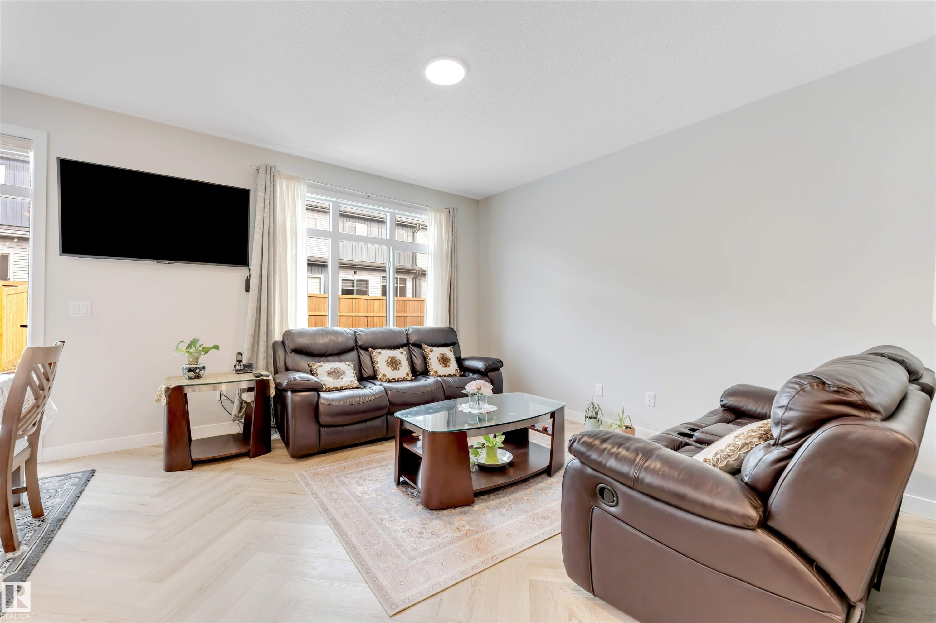 Living area featuring light wood-finish flooring with a herringbone pattern, recessed ceiling lighting, and large windows with white trim - 6404 27 Avenue, Edmonton, AB - Indoor Photo Showing Living Room