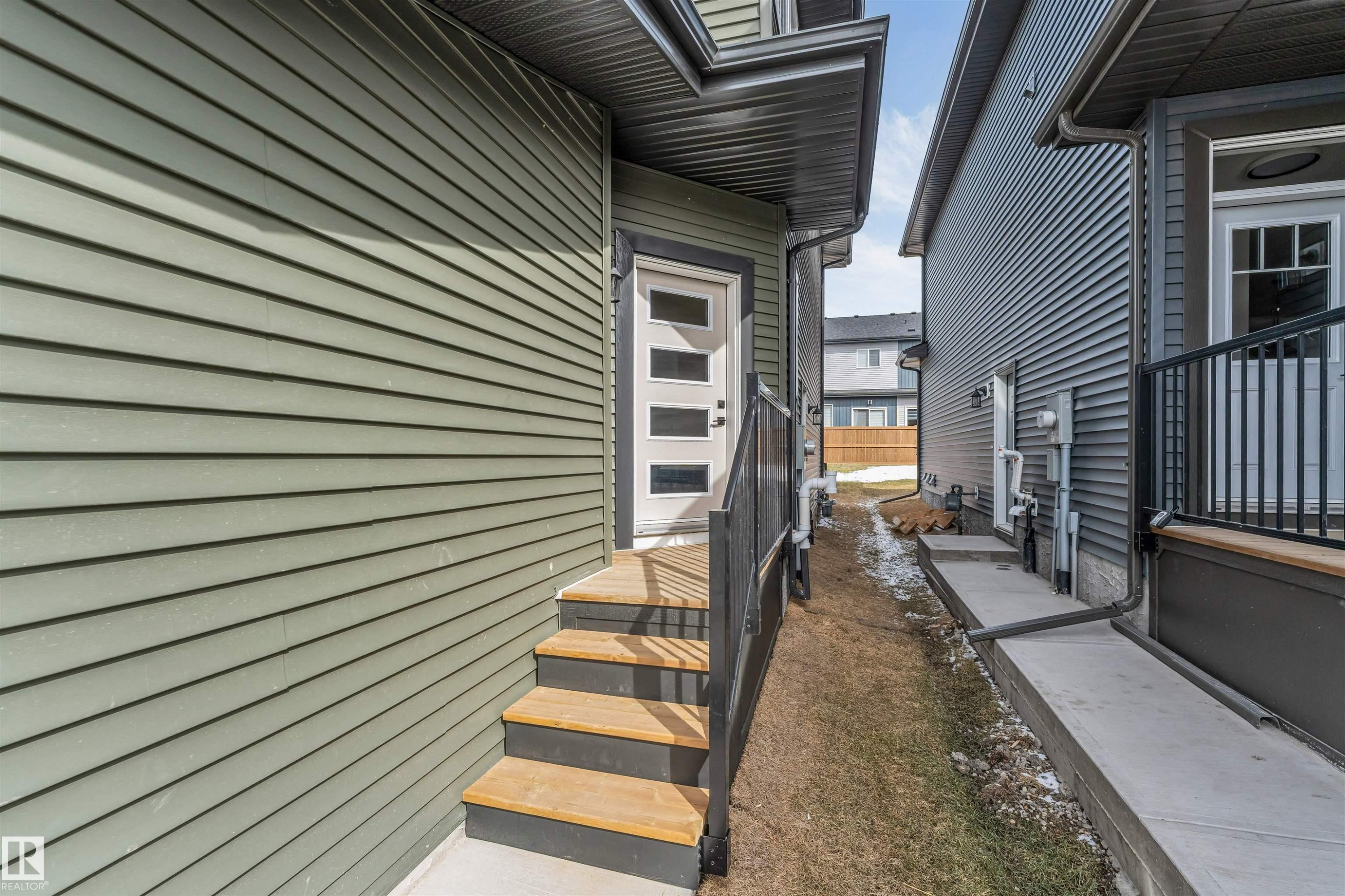 Rear exterior entrance featuring a modern white door with frosted glass panels, wood-finish stairs, and black metal railings - 6404 27 Avenue, Edmonton, AB - Outdoor With Exterior