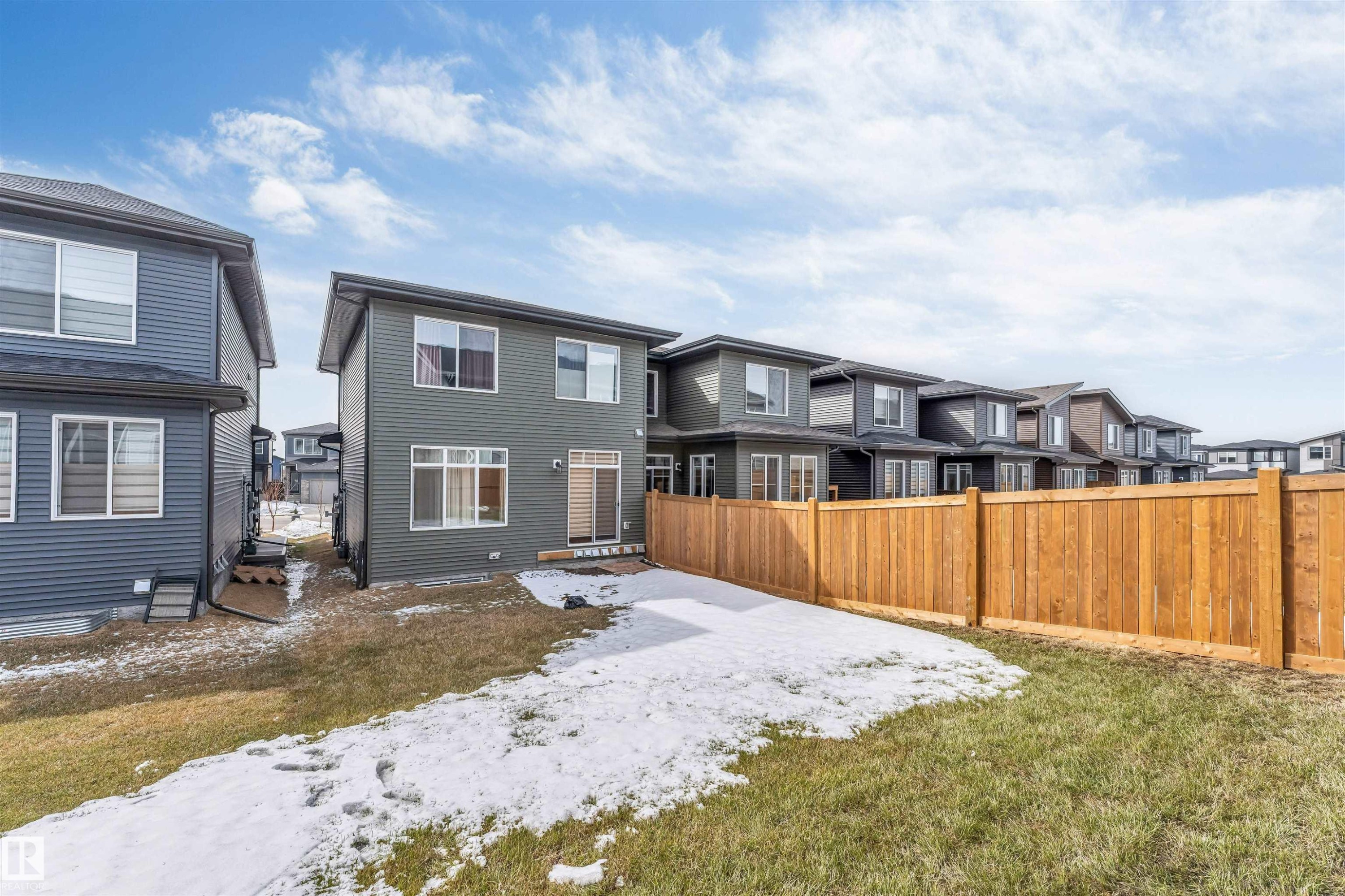 Rear exterior featuring a sliding glass door, multiple windows, a private wooden fence, and a partially grassed yard - 6404 27 Avenue, Edmonton, AB - Outdoor