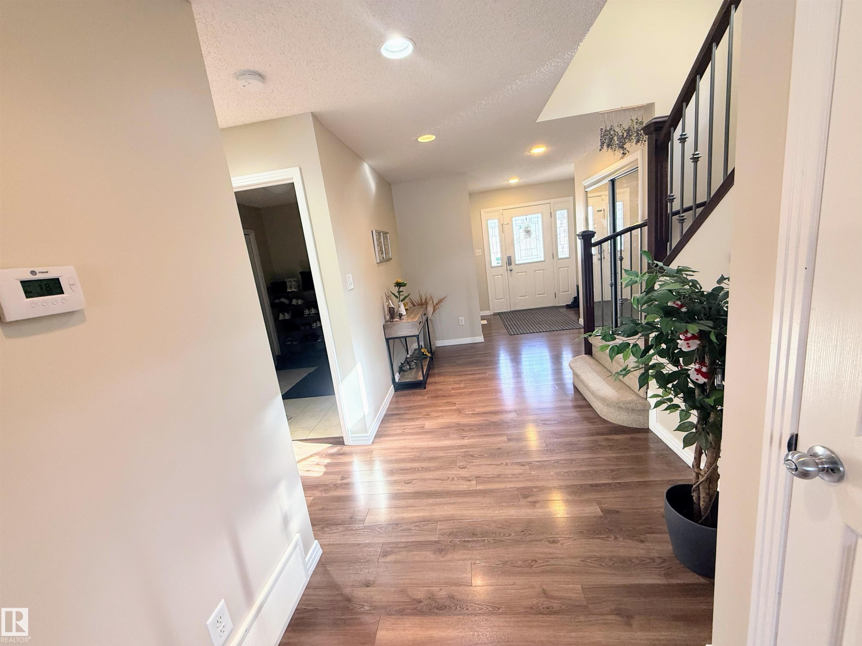 Inviting entryway featuring wood-finish flooring, a staircase with dark wood banister and wrought iron spindles, and recessed ceiling lighting - 3538 Claxton Crescent, Edmonton, AB - Indoor Photo Showing Other Room