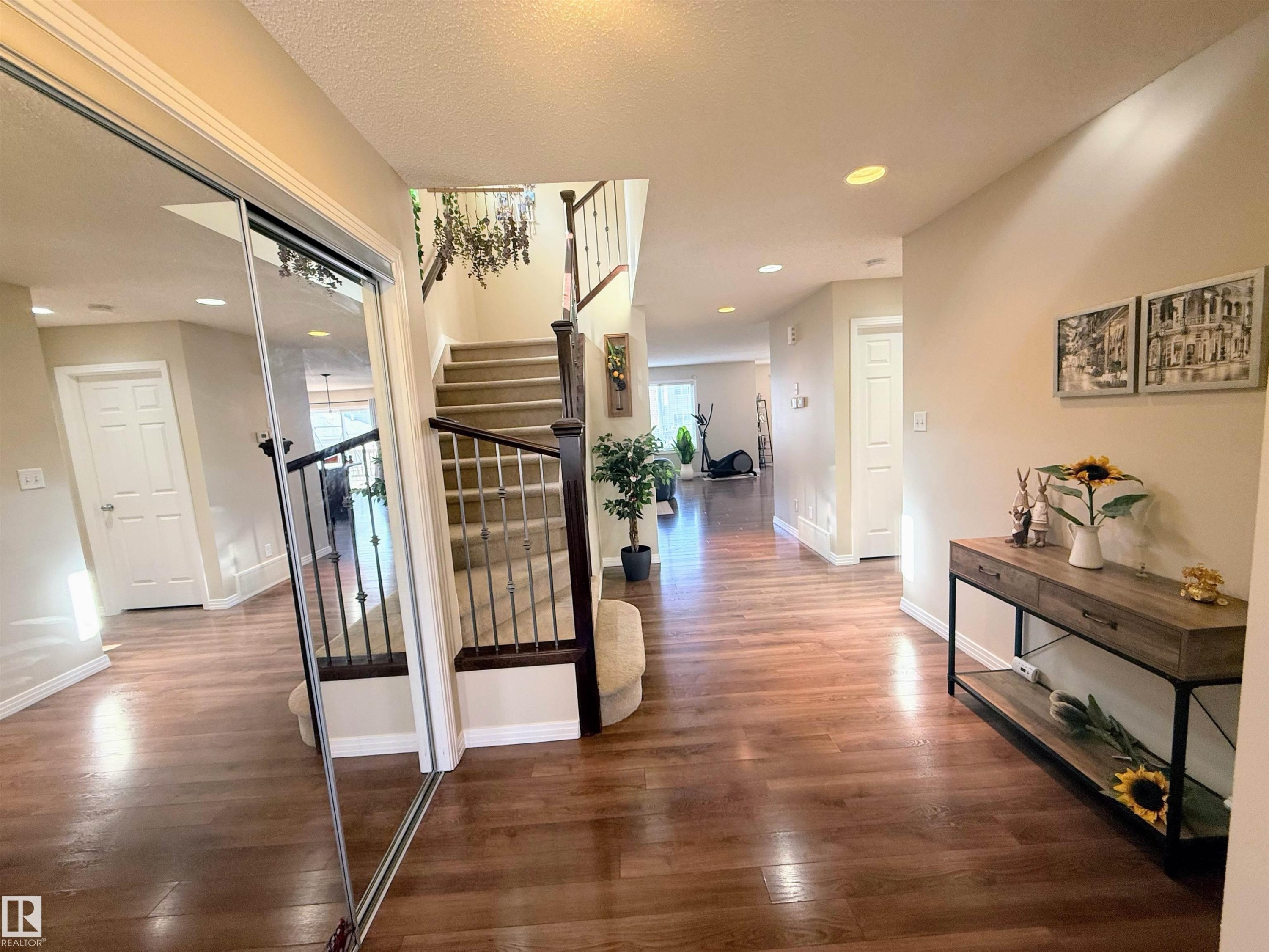 Spacious entryway featuring wood-finish flooring, a carpeted staircase with wrought iron balusters, recessed lighting, and a mirrored sliding closet door - 3538 Claxton Crescent, Edmonton, AB - Indoor Photo Showing Other Room