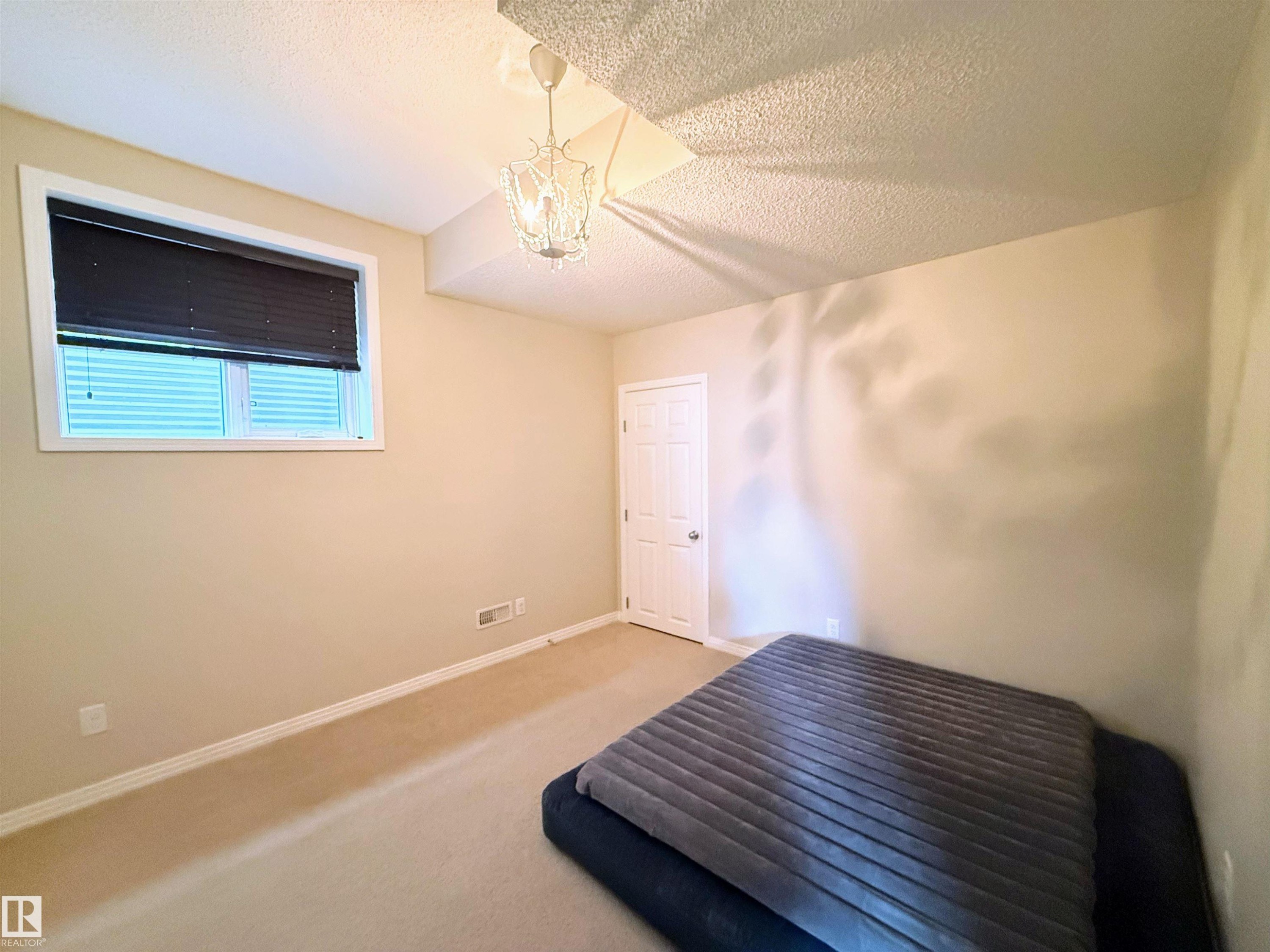 Carpeted room with a white door, a window with horizontal blinds, and a decorative ceiling light fixture - 3538 Claxton Crescent, Edmonton, AB - Indoor