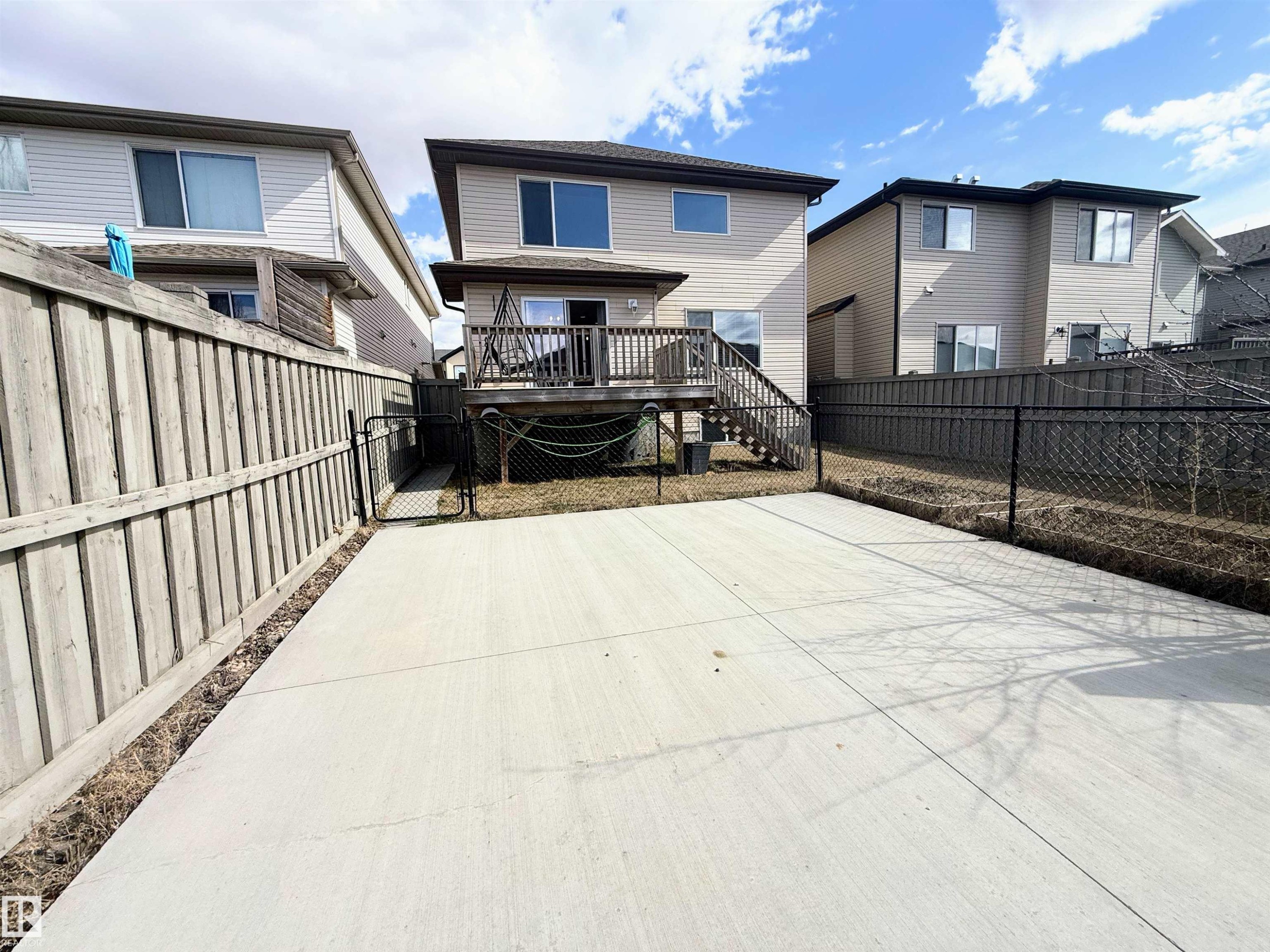 Rear exterior featuring a raised wooden deck with stairs, vinyl siding, and a concrete patio - 3538 Claxton Crescent, Edmonton, AB - Outdoor With Exterior