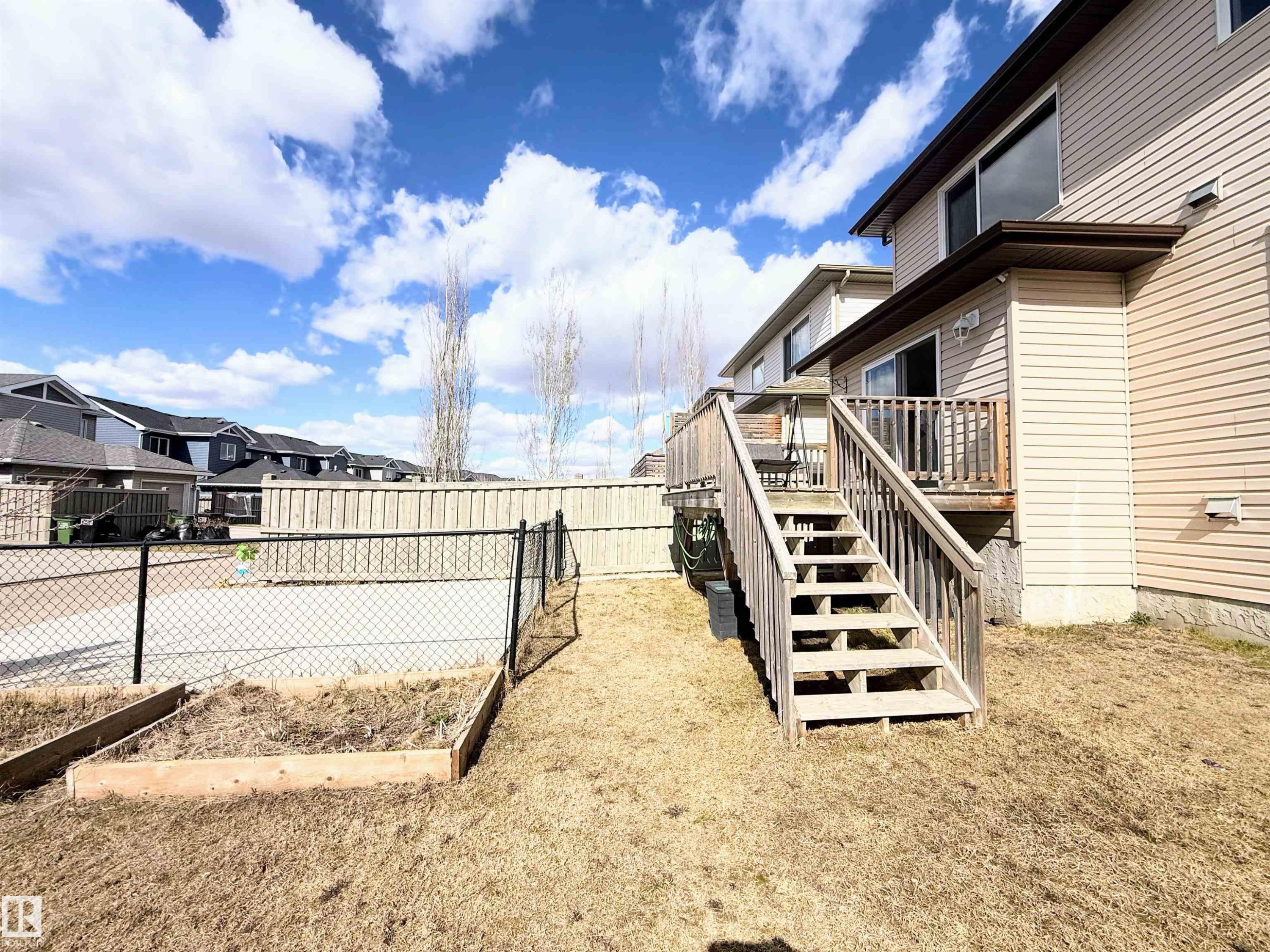 Rear exterior featuring a wood deck with stairs, beige vinyl siding, and a sliding glass door - 3538 Claxton Crescent, Edmonton, AB - Outdoor With Exterior