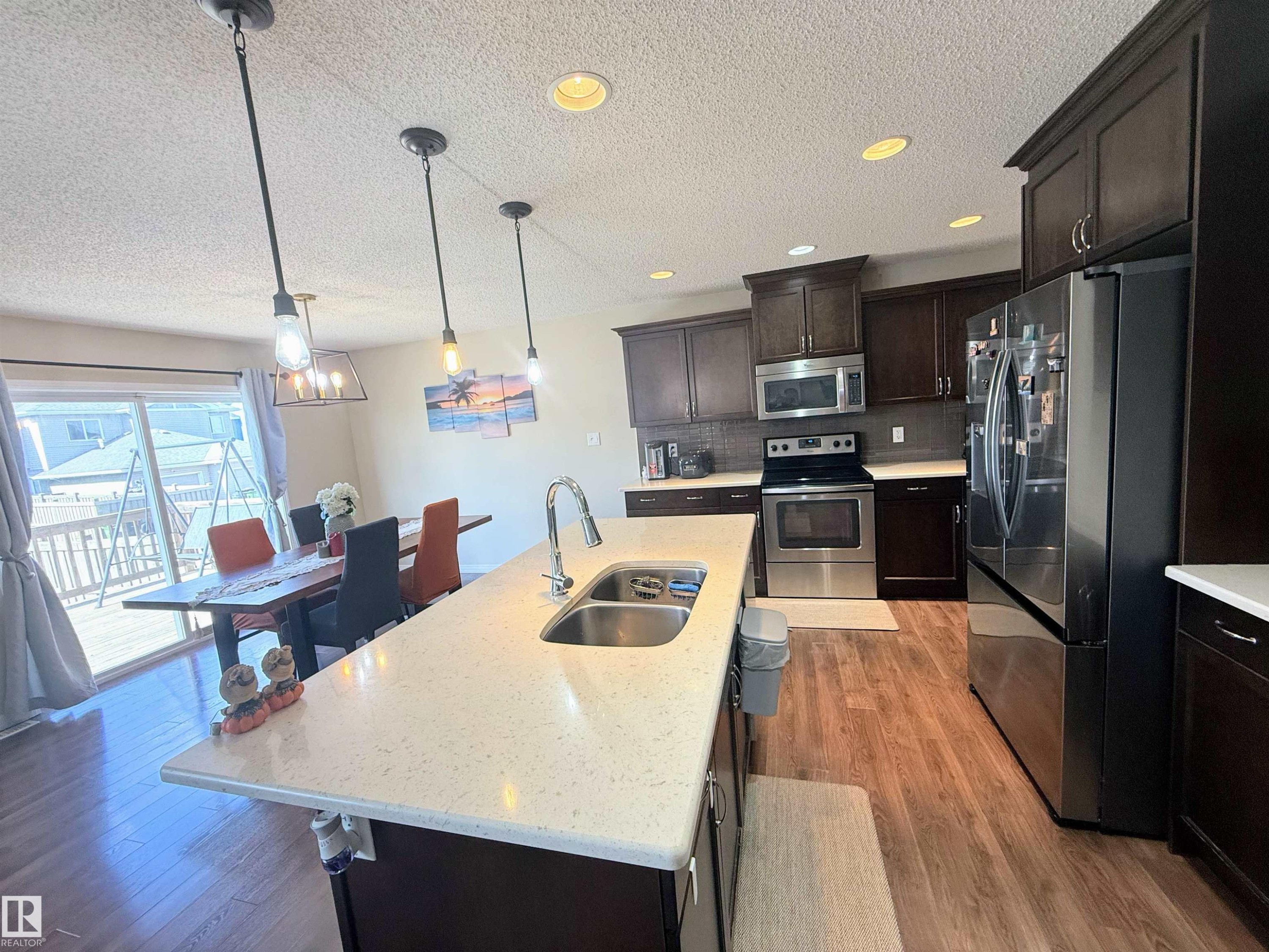 Kitchen featuring dark wood cabinetry, stainless steel appliances, a center island with a double basin sink, light-toned countertops, and wood-finish flooring - 3538 Claxton Crescent, Edmonton, AB - Indoor Photo Showing Kitchen With Stainless Steel Kitchen With Double Sink With Upgraded Kitchen