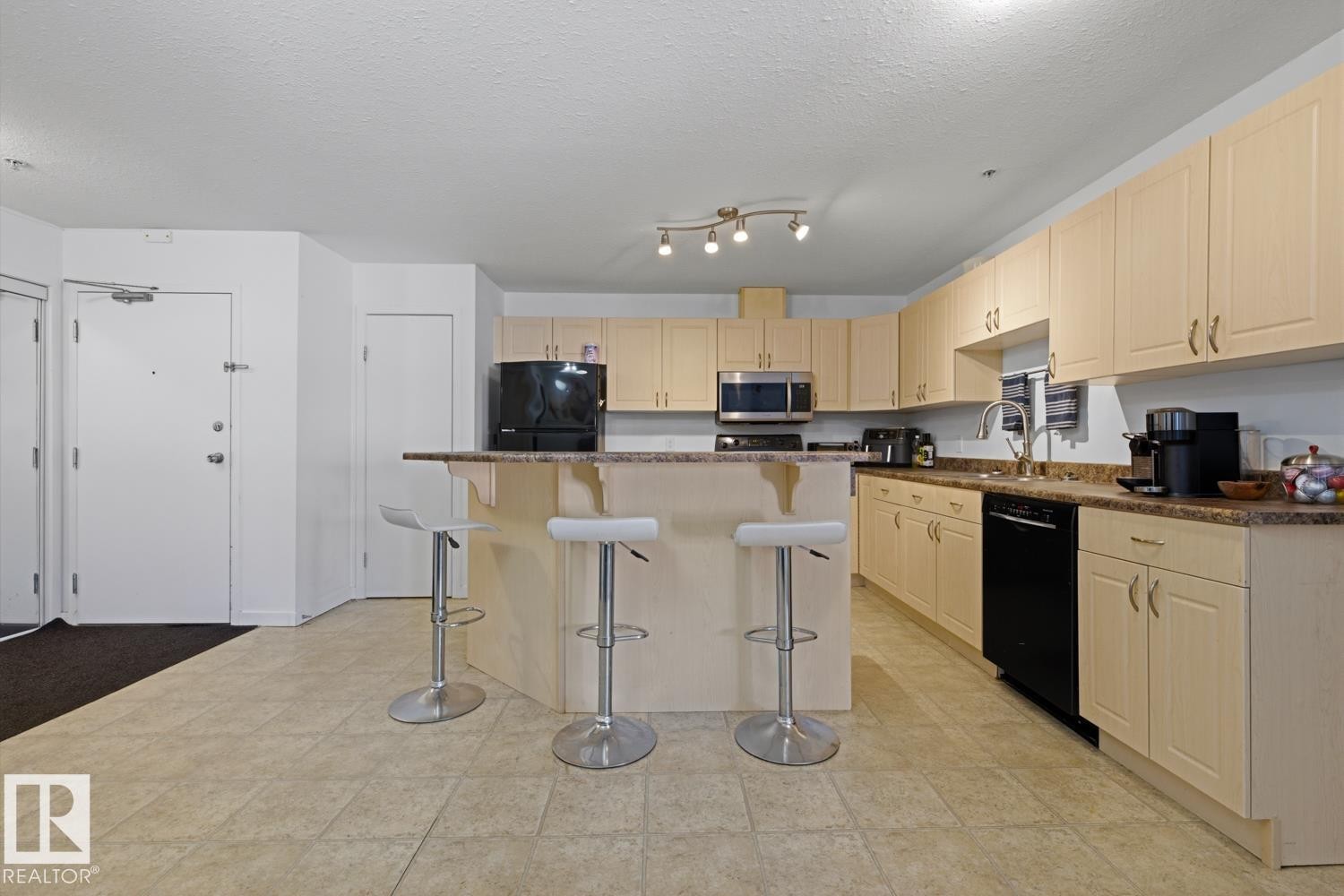 Kitchen featuring a breakfast bar with seating, extensive light wood-finish cabinetry, black appliances, and speckled countertops - 304 4312 139 Ave, Edmonton, AB - Indoor Photo Showing Kitchen