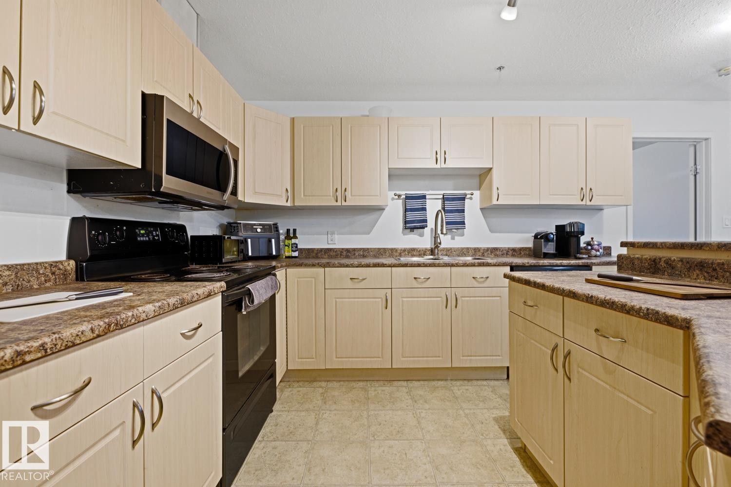 Expansive kitchen featuring light wood-finish cabinetry, patterned countertops, and tile flooring - 304 4312 139 Ave, Edmonton, AB - Indoor Photo Showing Kitchen