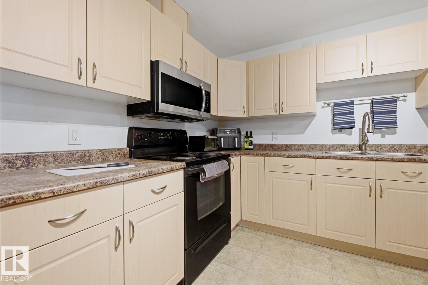 Kitchen featuring light-toned cabinetry, laminate countertops, a stainless steel microwave, a black electric range, and a stainless steel sink with a gooseneck faucet - 304 4312 139 Ave, Edmonton, AB - Indoor Photo Showing Kitchen