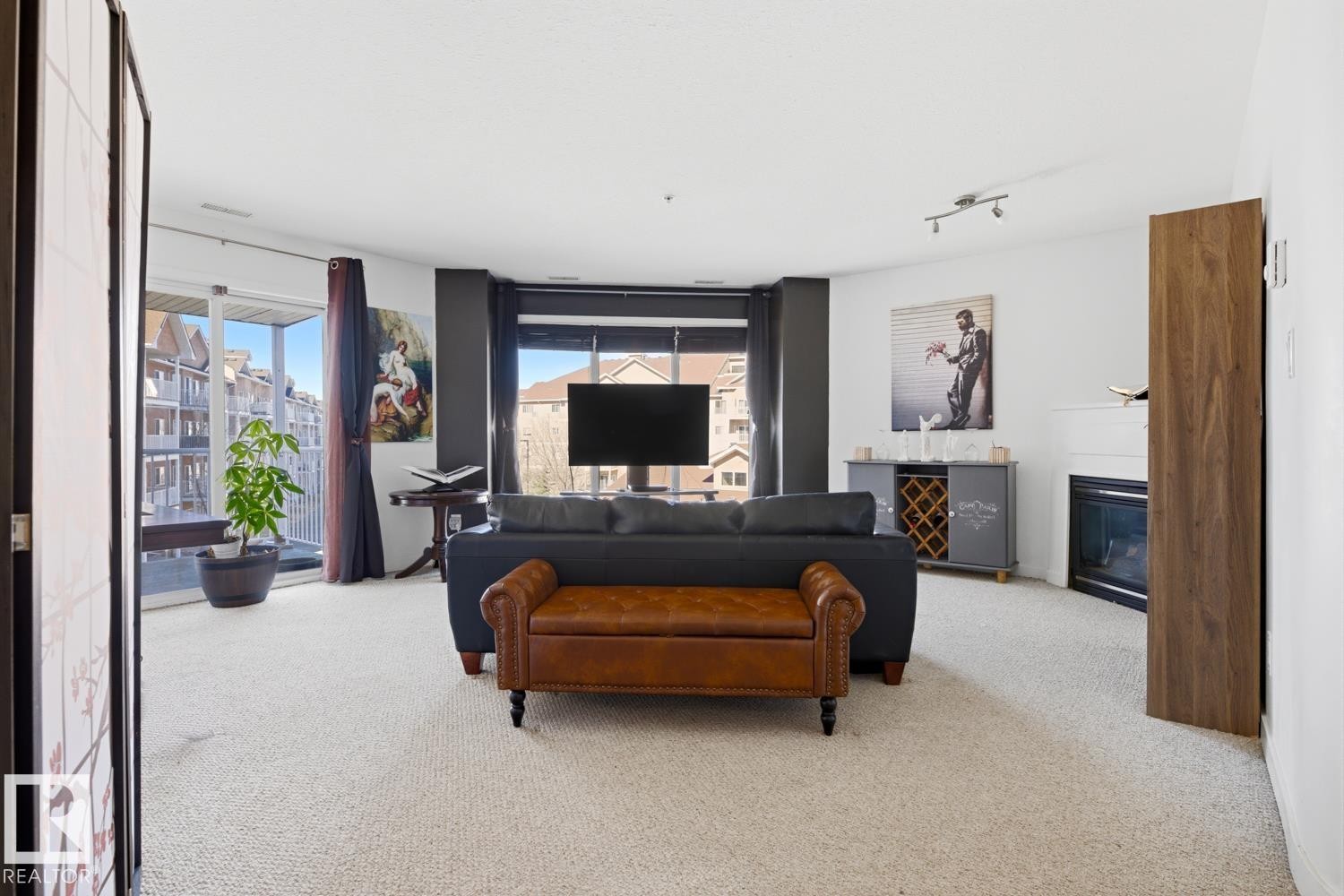 Carpeted living space featuring a built-in fireplace, track lighting, and outdoor balcony access through sliding glass doors - 304 4312 139 Ave, Edmonton, AB - Indoor Photo Showing Living Room With Fireplace