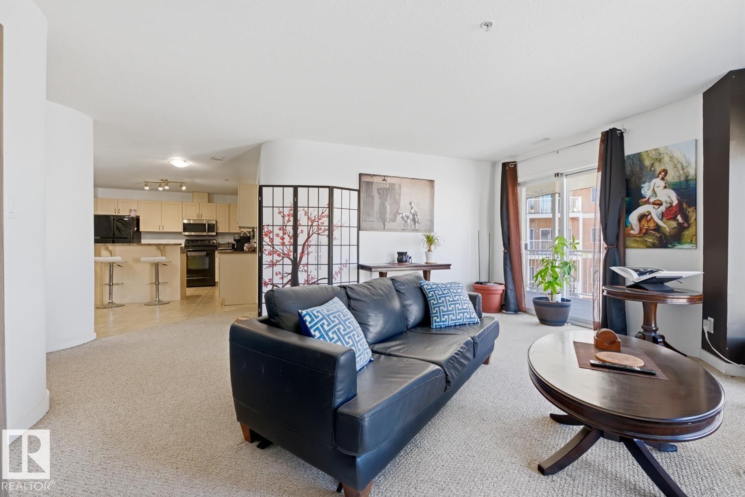 Living area with neutral carpeting, an open concept layout, light-toned kitchen cabinetry, dark appliances, and a glass-paneled patio door - 304 4312 139 Ave, Edmonton, AB - Indoor Photo Showing Living Room