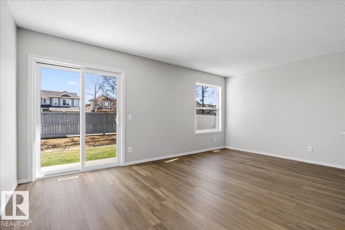 Spacious room with wood-finish flooring, light grey painted walls, and a textured white ceiling - #7 18004 89 St Nw, Edmonton, AB - Indoor
