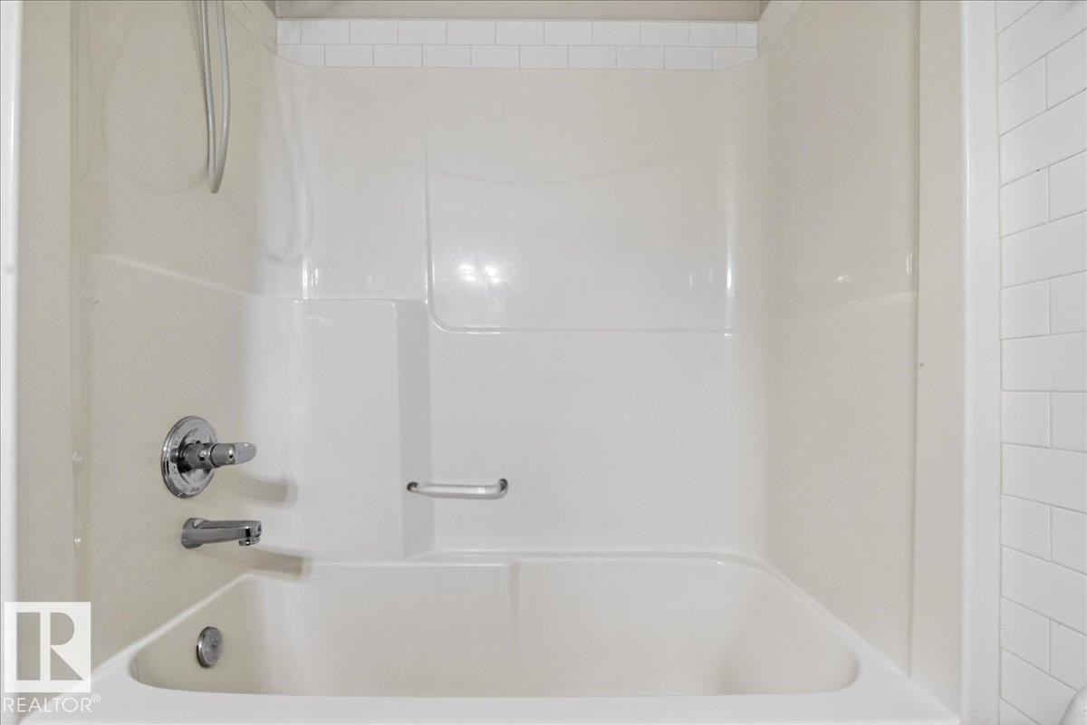 White bathtub with integrated shower surround, chrome fixtures, and a recessed soap dish - #7 18004 89 St Nw, Edmonton, AB - Indoor Photo Showing Bathroom