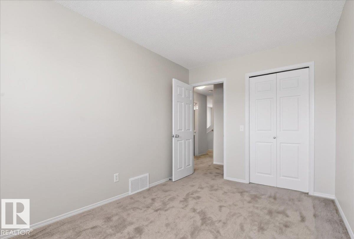 Light gray painted walls, textured ceiling, light gray carpet, white baseboards, and white bi-fold closet doors - #7 18004 89 St Nw, Edmonton, AB - Indoor Photo Showing Other Room