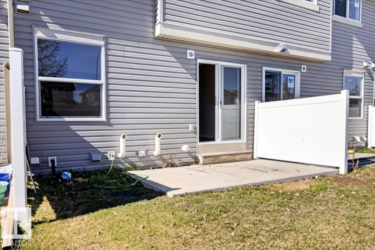 Patio area featuring a concrete slab, sliding glass door entry, and a white privacy fence - #7 18004 89 St Nw, Edmonton, AB - Outdoor With Exterior