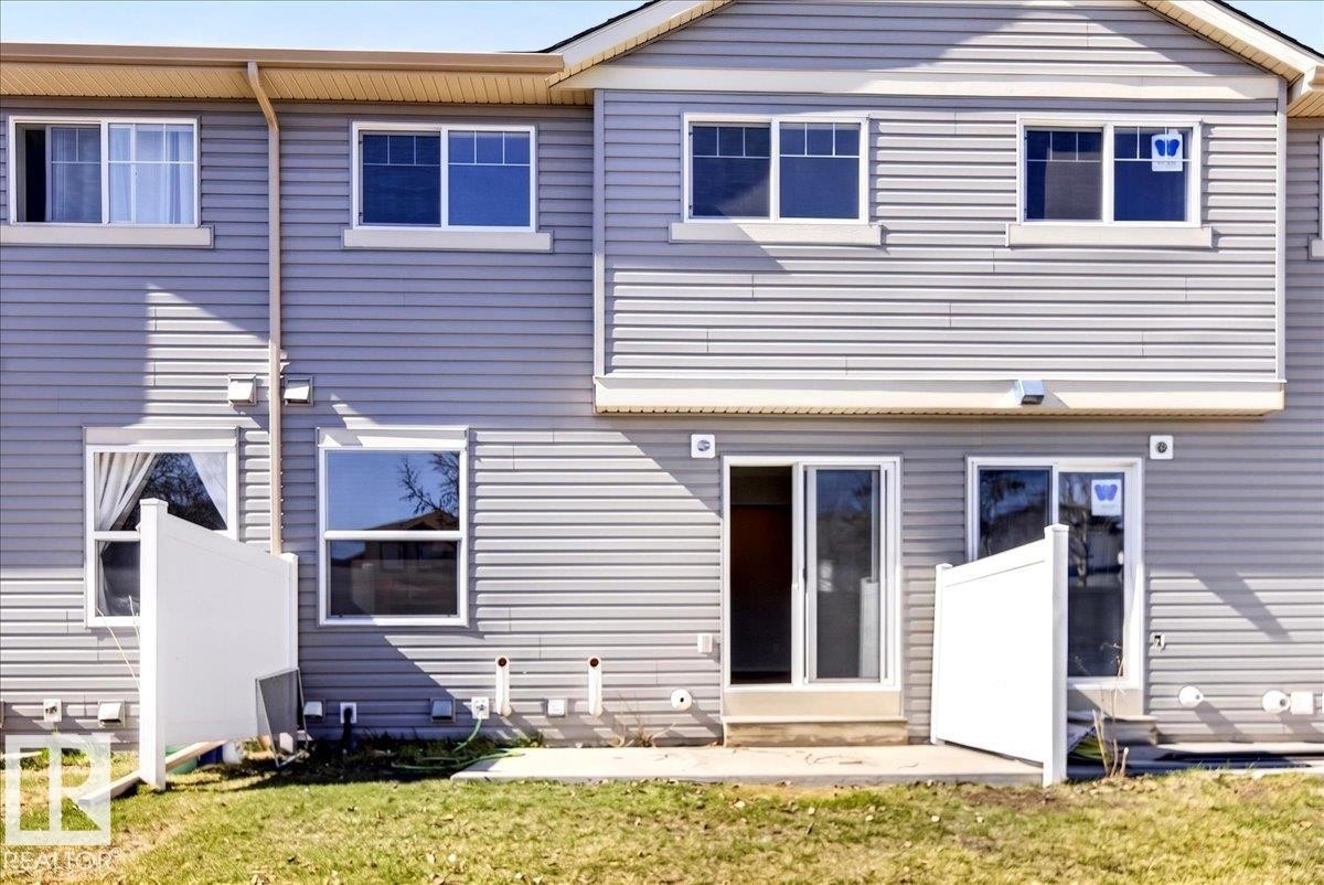 Gray horizontal siding exterior featuring multiple windows, two sliding glass doors, and a small concrete patio - #7 18004 89 St Nw, Edmonton, AB - Outdoor With Exterior
