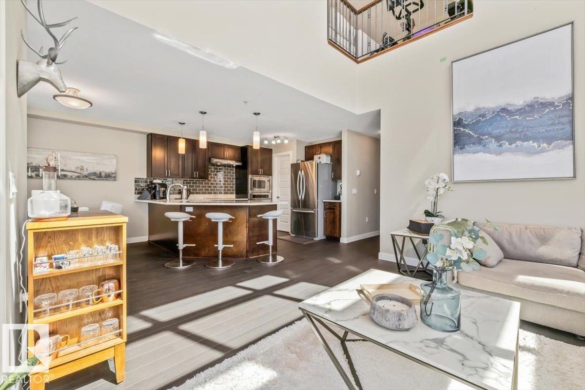 Kitchen featuring dark wood cabinetry, light-toned countertops, and a reflective subway tile backsplash - 513 1230 Windermere Way, Edmonton, AB