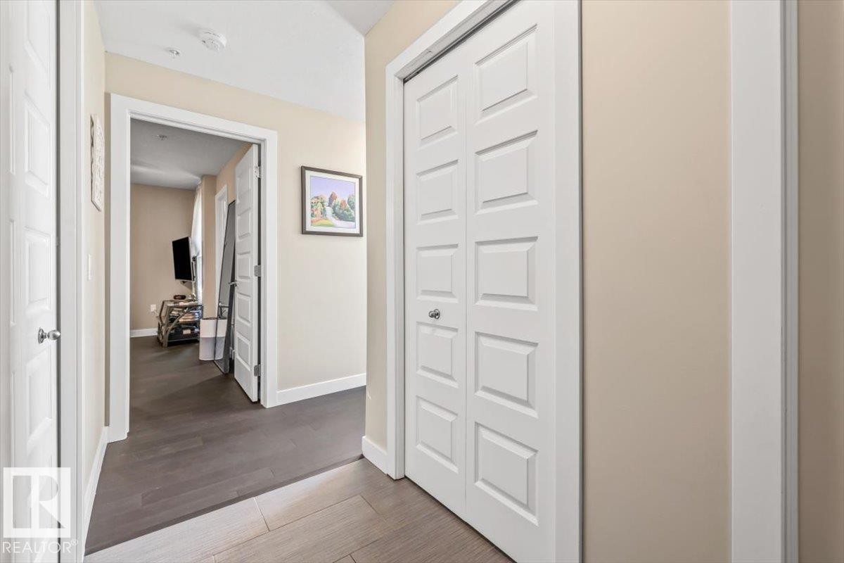 Living area featuring soaring two-story windows with dark framing, rich wood-finish flooring, and a private balcony with glass railing - 513 1230 Windermere Way, Edmonton, AB