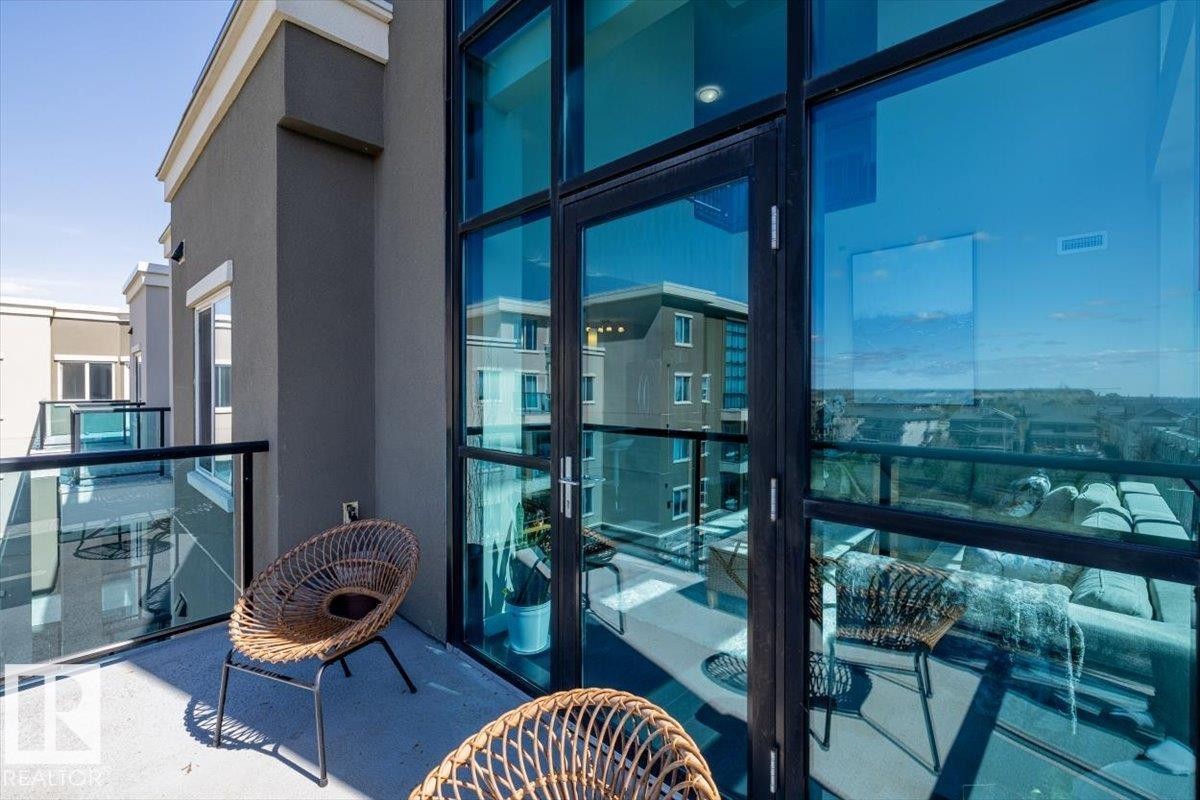 Two-story living area featuring dark wood-finish flooring, a full wall of floor-to-ceiling windows with black frames, and an open-tread staircase with metal railings - 513 1230 Windermere Way, Edmonton, AB
