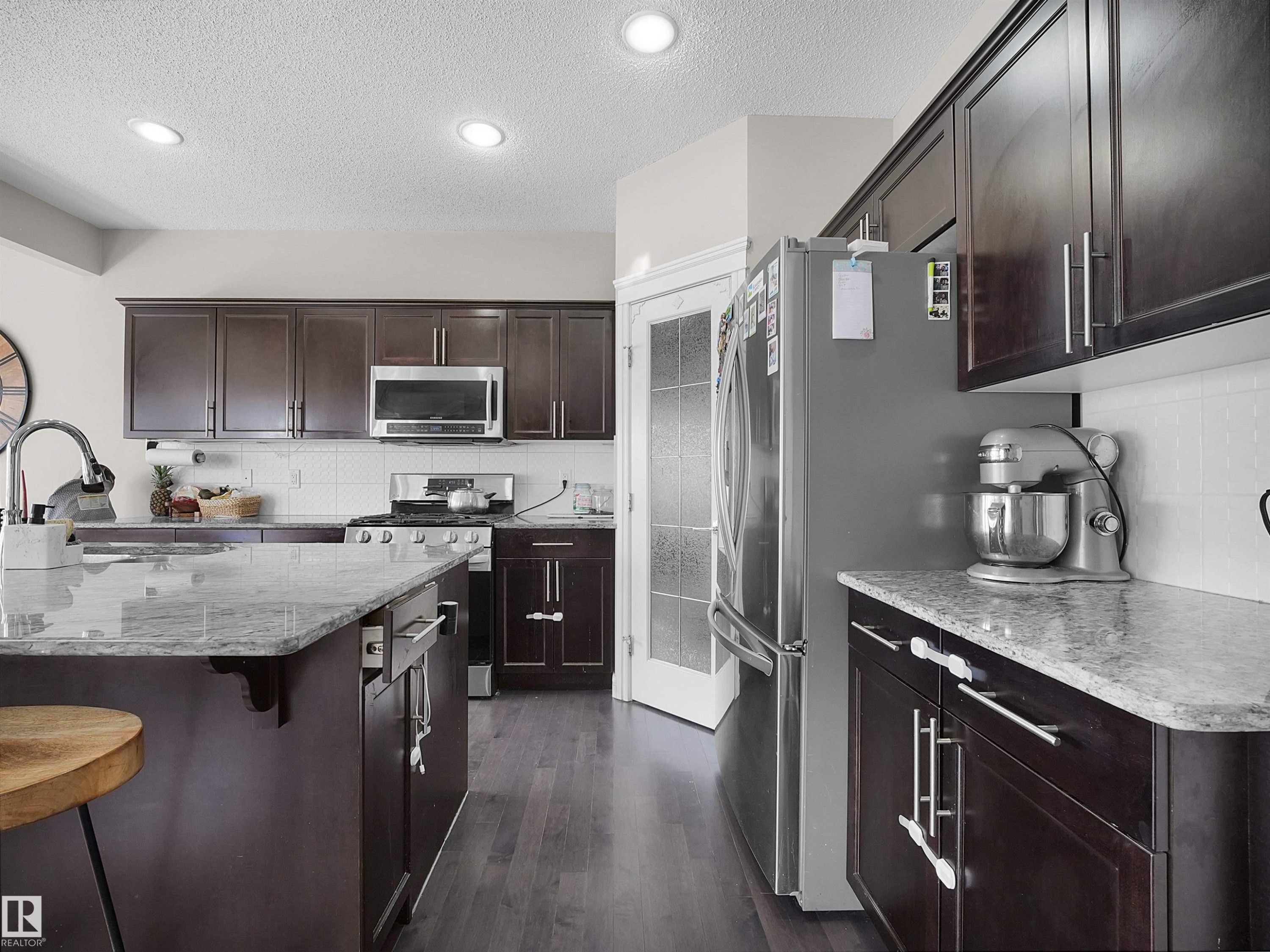 Kitchen featuring recessed lighting, dark wood-finish cabinetry, stainless steel appliances, a white subway tile backsplash, and light-toned countertop surfaces - 3247 15 Avenue Nw, Edmonton, AB