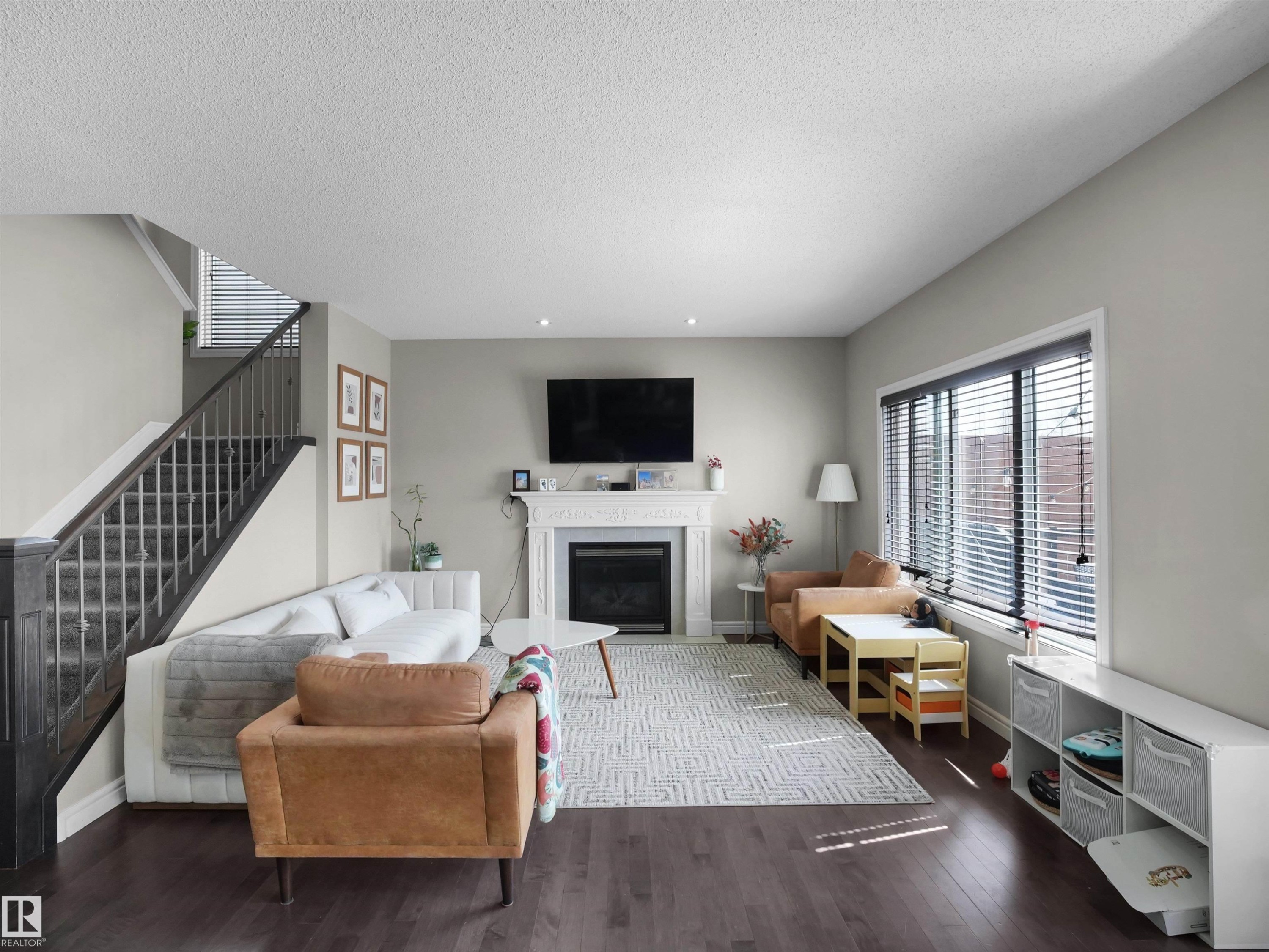 Spacious living area featuring a fireplace with a decorative mantel, dark wood-finish flooring, and a staircase with dark wood railings - 3247 15 Avenue Nw, Edmonton, AB